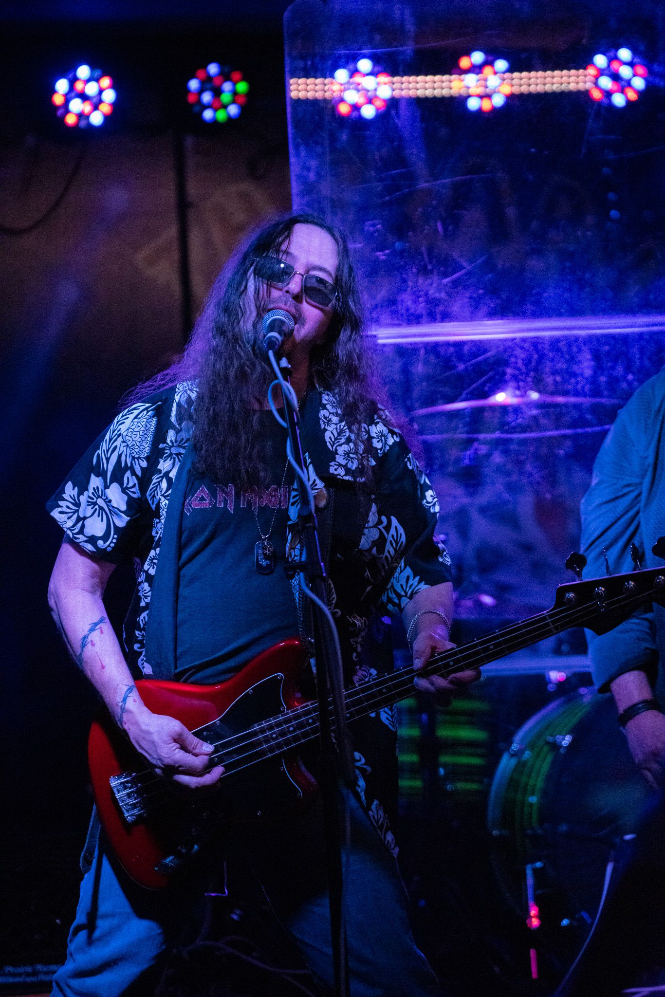 Bass guitarist performs under blue stage lighting with LED displays in background.