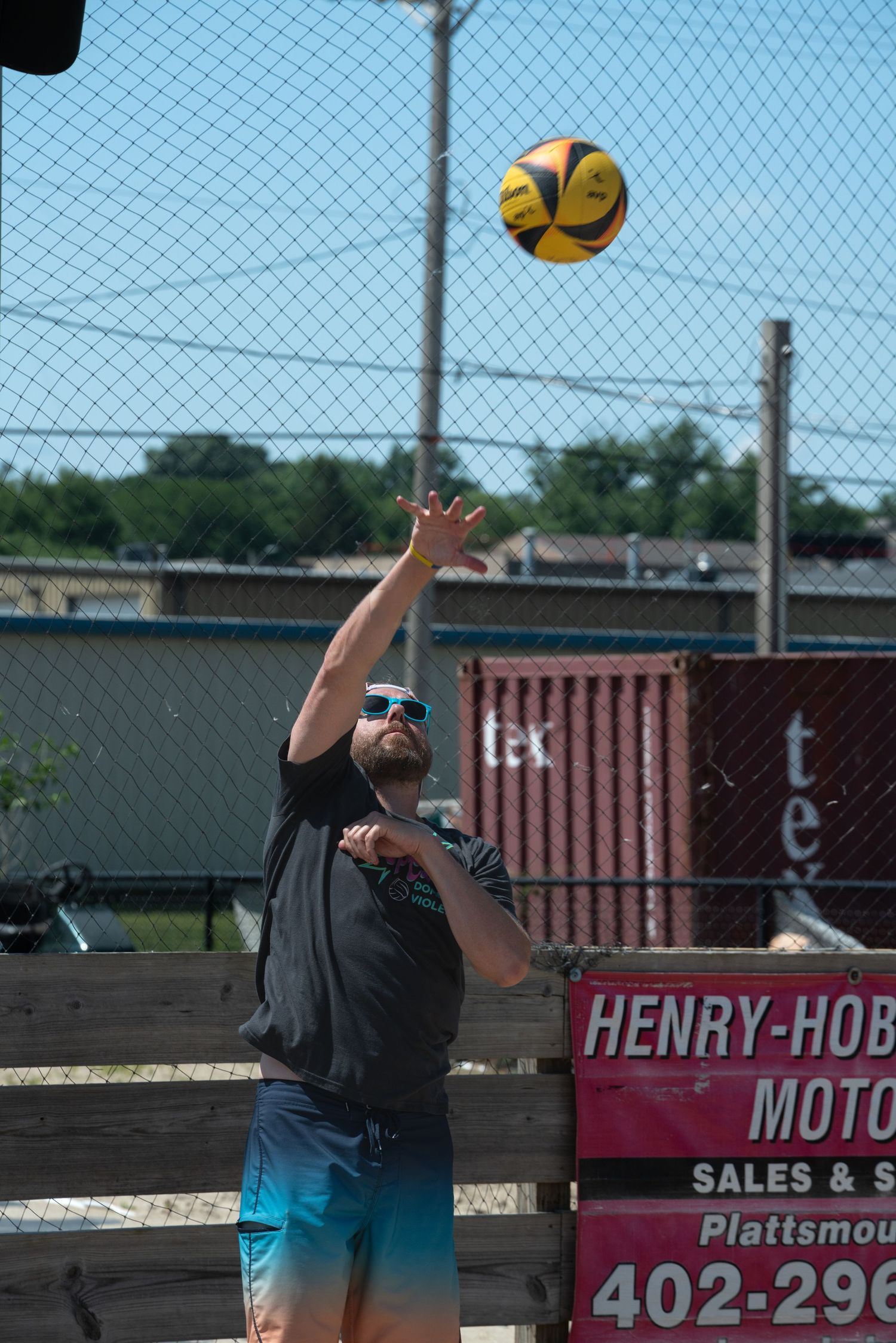Player reaching up to hit a yellow volleyball against blue sky background.