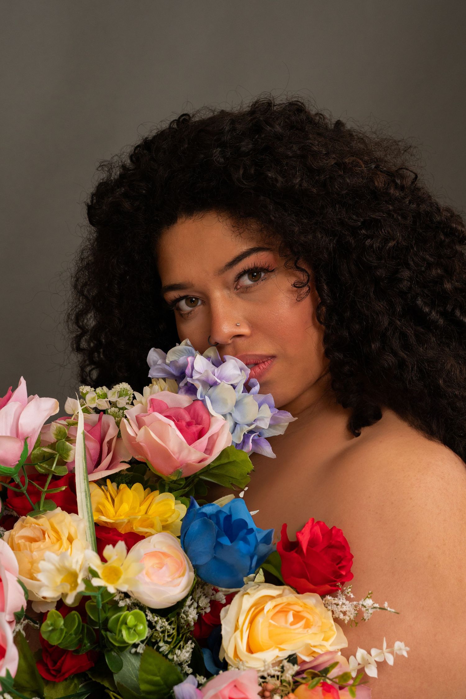 Close-up portrait with vibrant mixed flower bouquet against dark background.