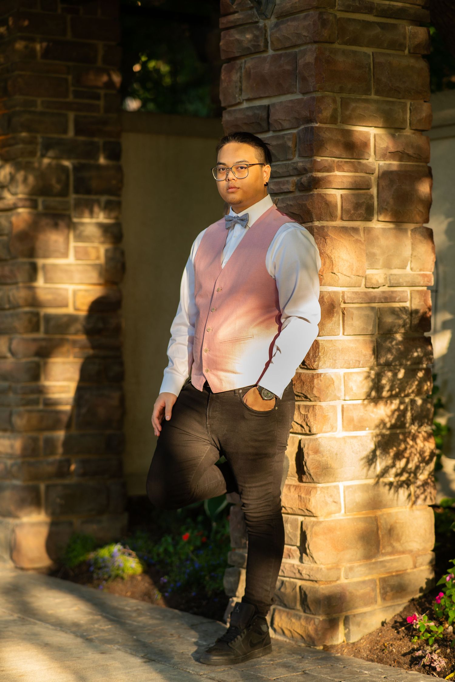Person in pink vest and white shirt poses against stone brick wall in dappled sunlight.