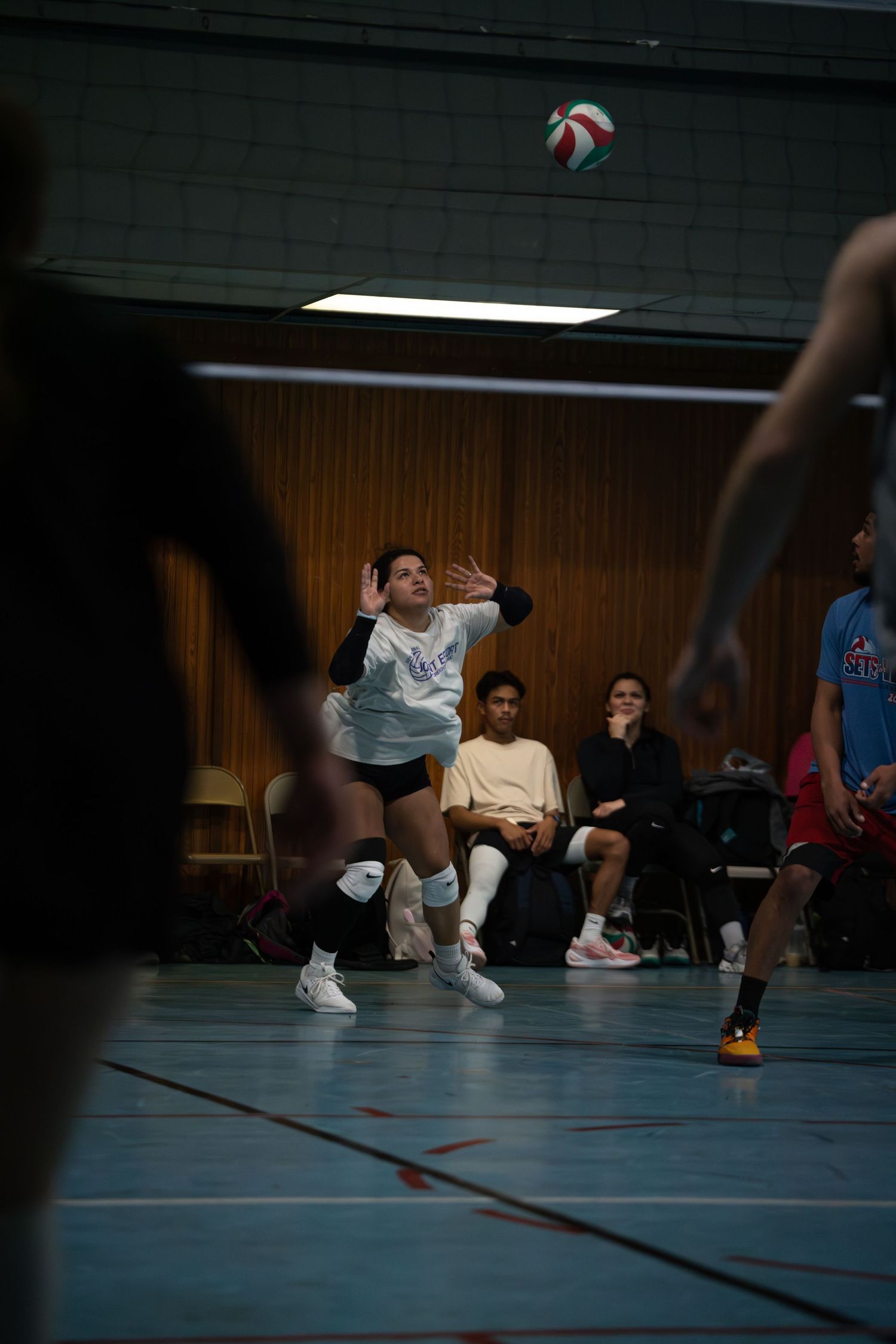 Players diving for volleyball during an indoor match on blue court.