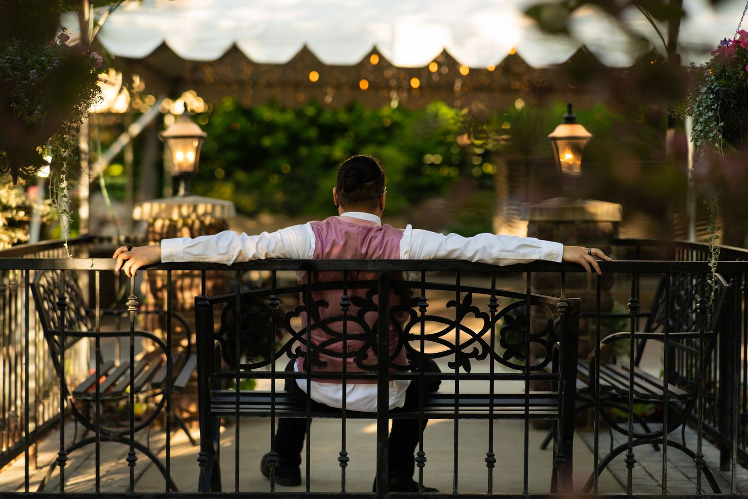 Silhouette of someone lying across a decorative metal bench during golden hour.