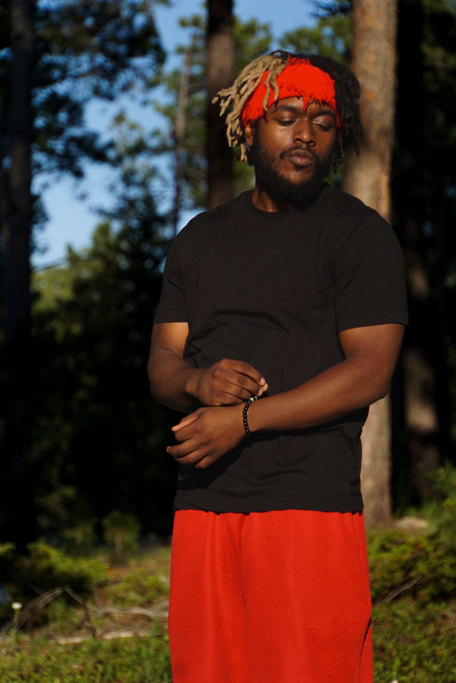 Person in black shirt and red pants stands confidently in outdoor forest setting.
