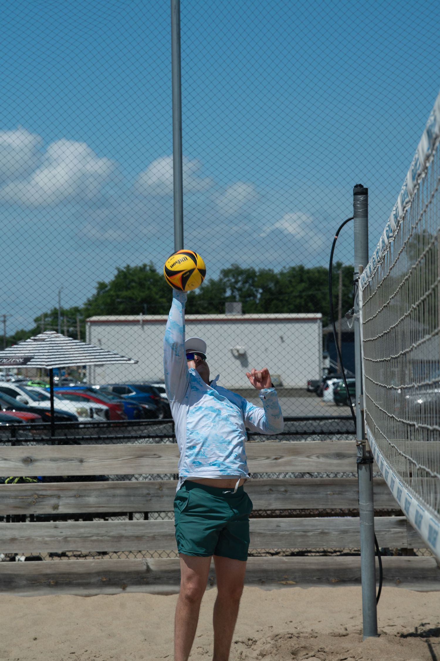 Person in blue shorts playing volleyball near a chain link fence.