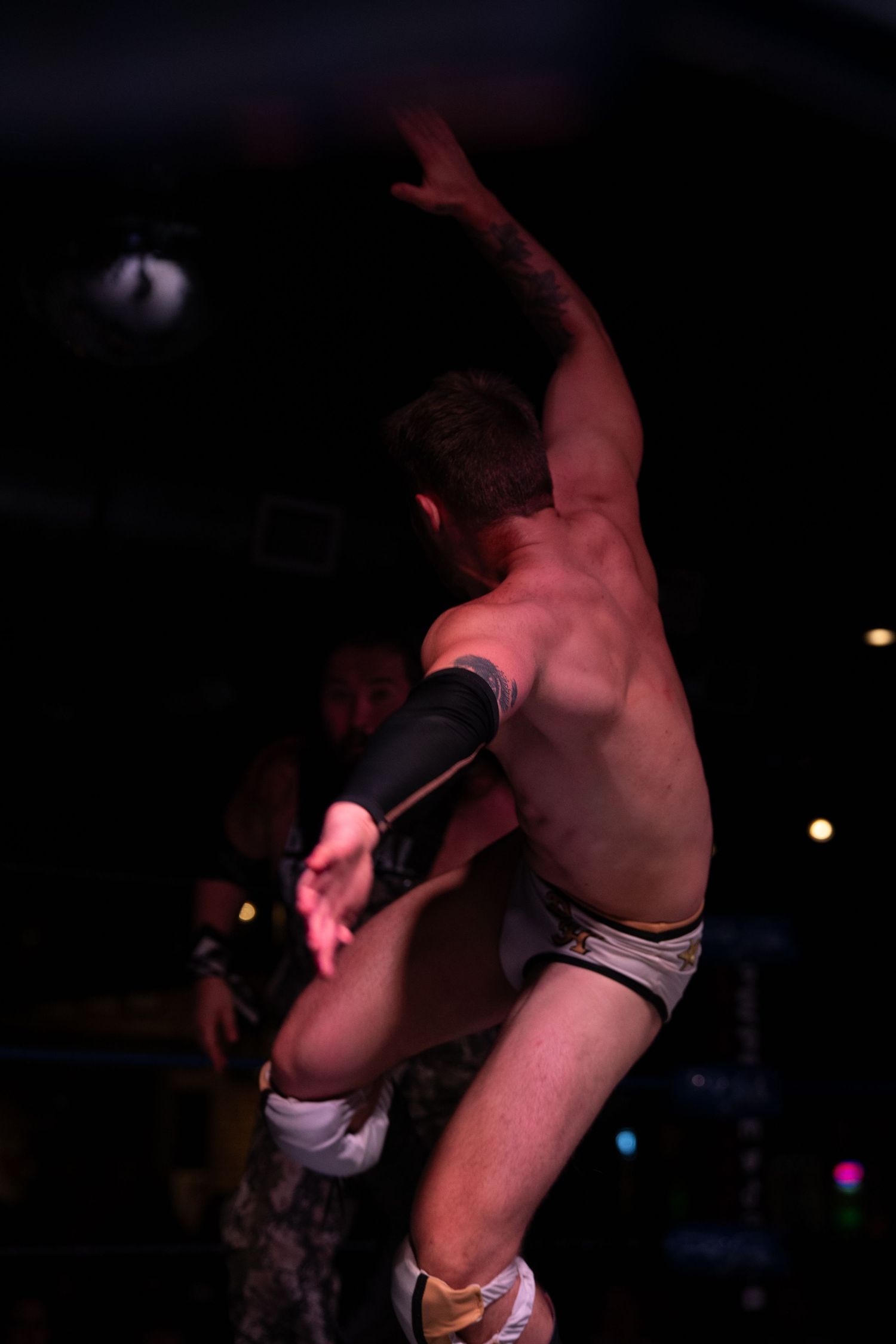 Professional wrestling match features an impressive aerial maneuver in a dark arena setting.