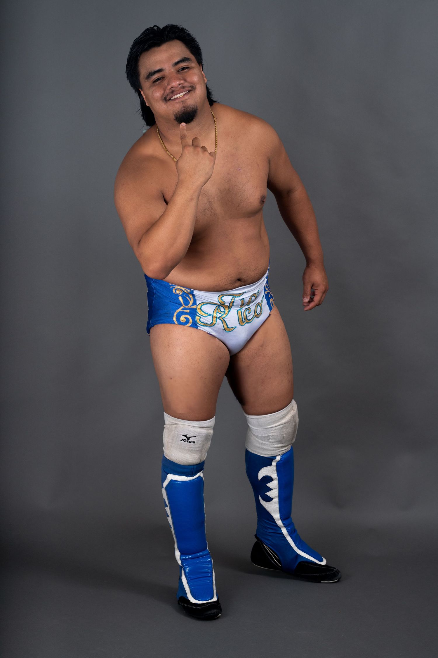 Studio portrait in blue and white wrestling attire against grey background.