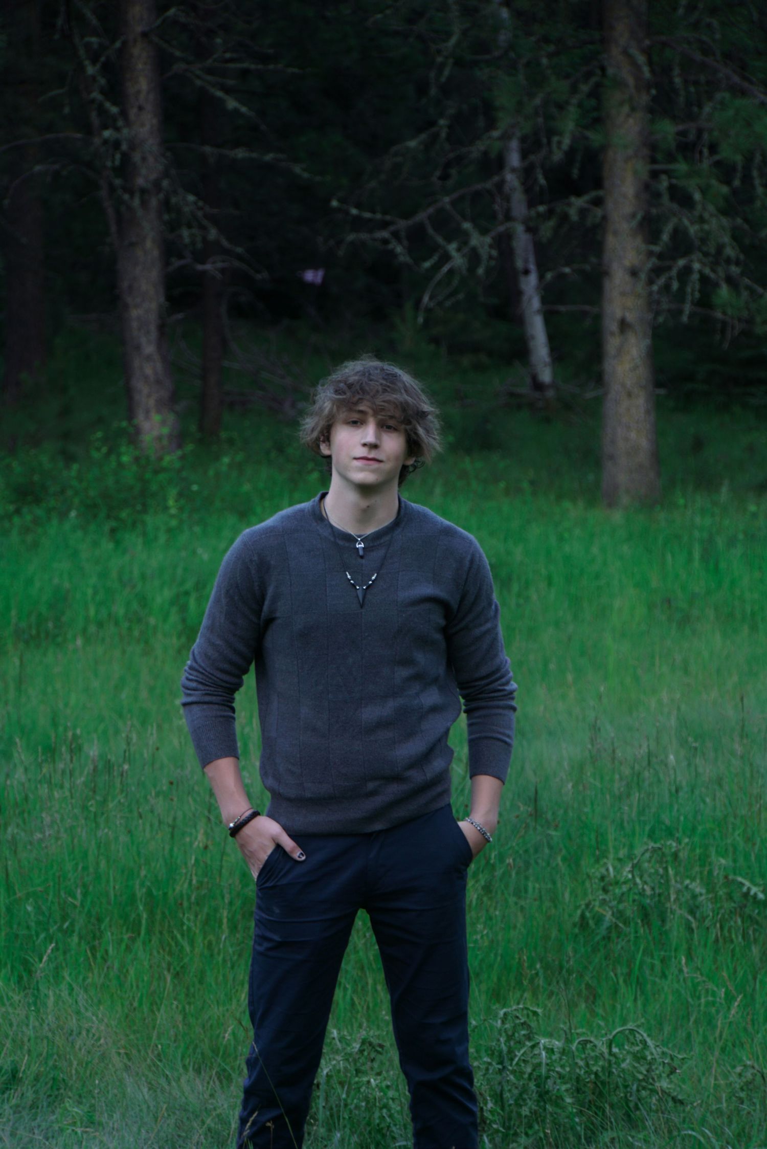 Figure in dark clothing stands in a grassy field with trees in the background.