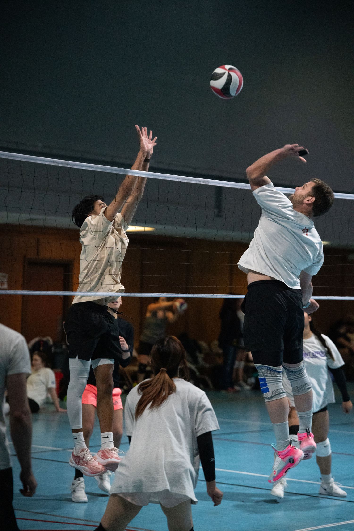 Players jump to hit a volleyball during an indoor recreational game.