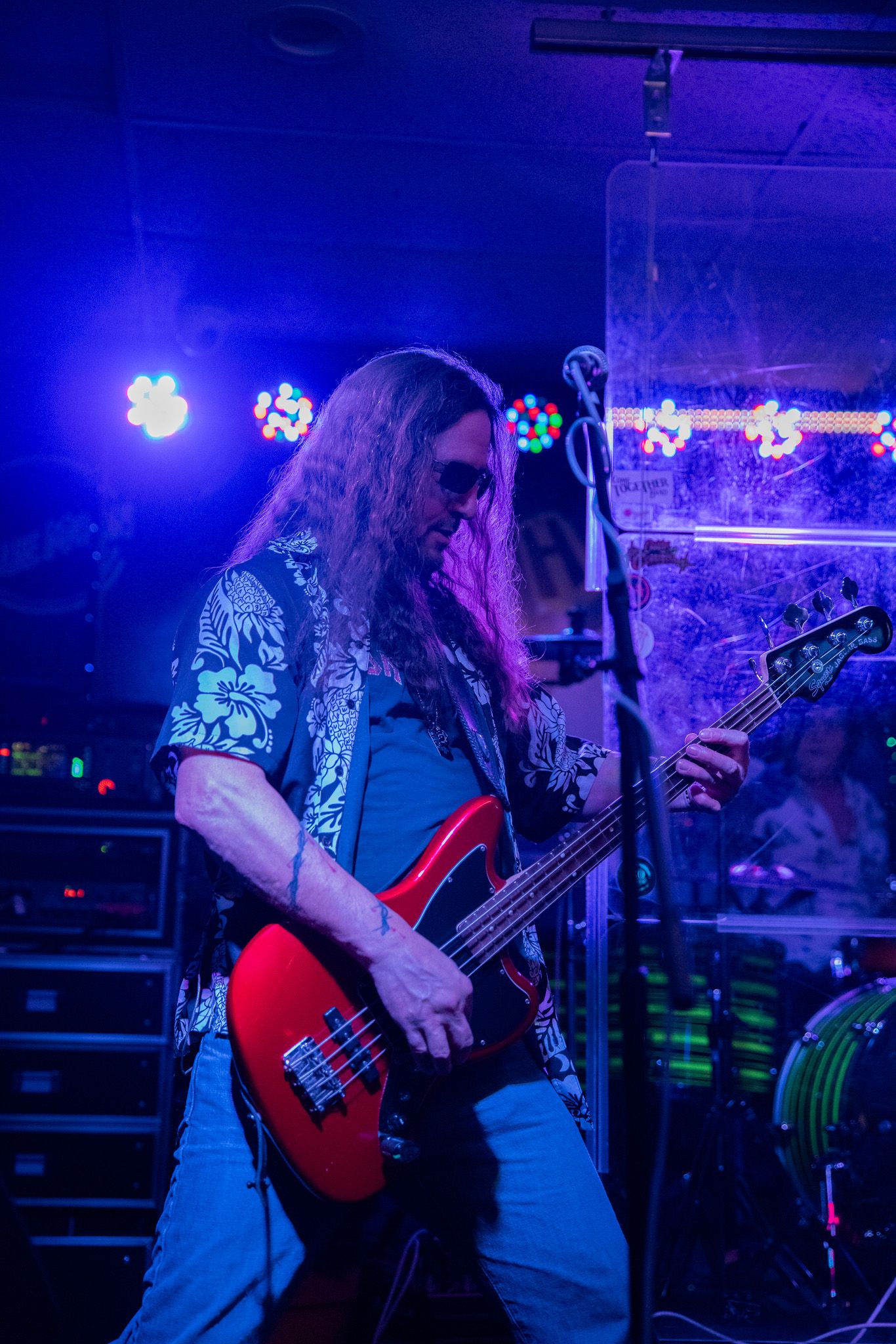 Bassist plays a red guitar on stage illuminated by deep blue lights.