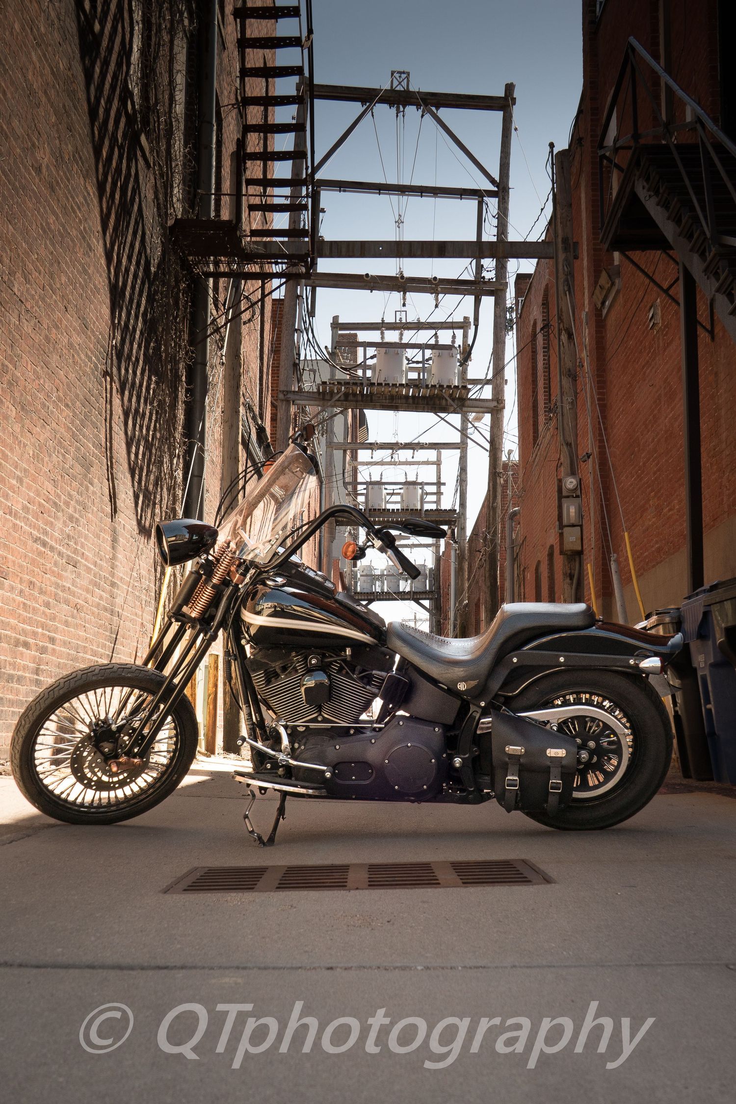 Custom motorcycle photographed in an industrial brick alley with dramatic lighting and shadows.
