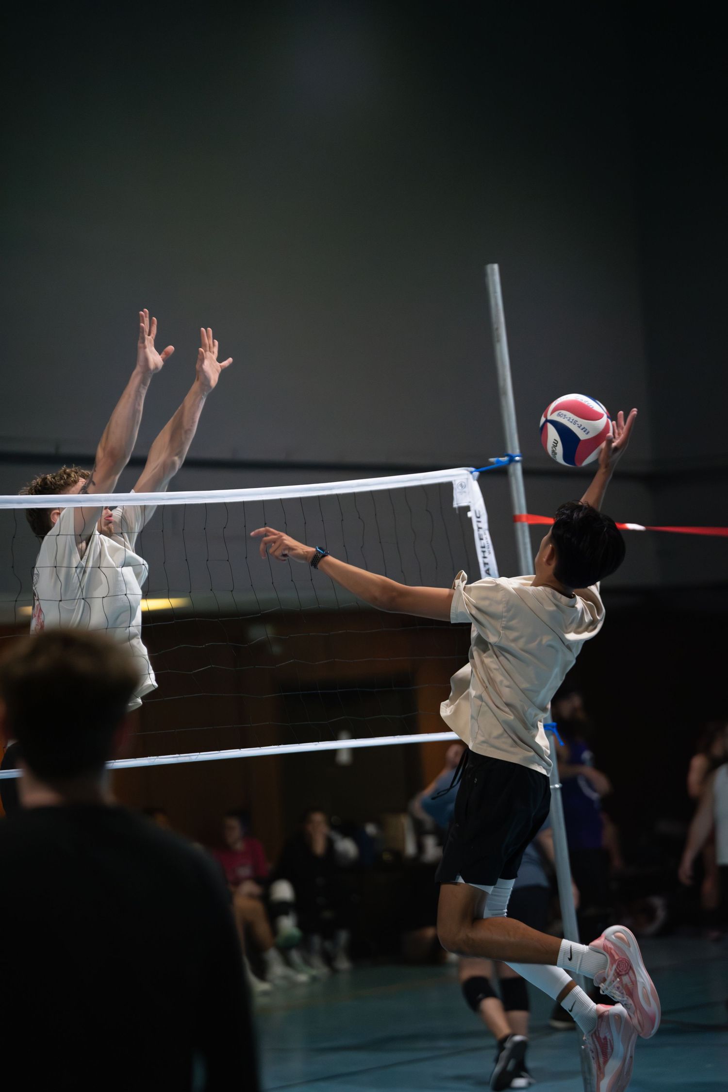 Athletes jump to block a volleyball shot during an indoor match.
