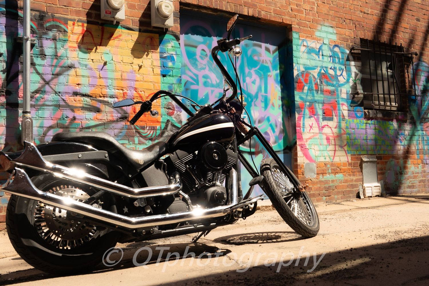 Custom motorcycles parked against a brick wall covered in colorful graffiti.