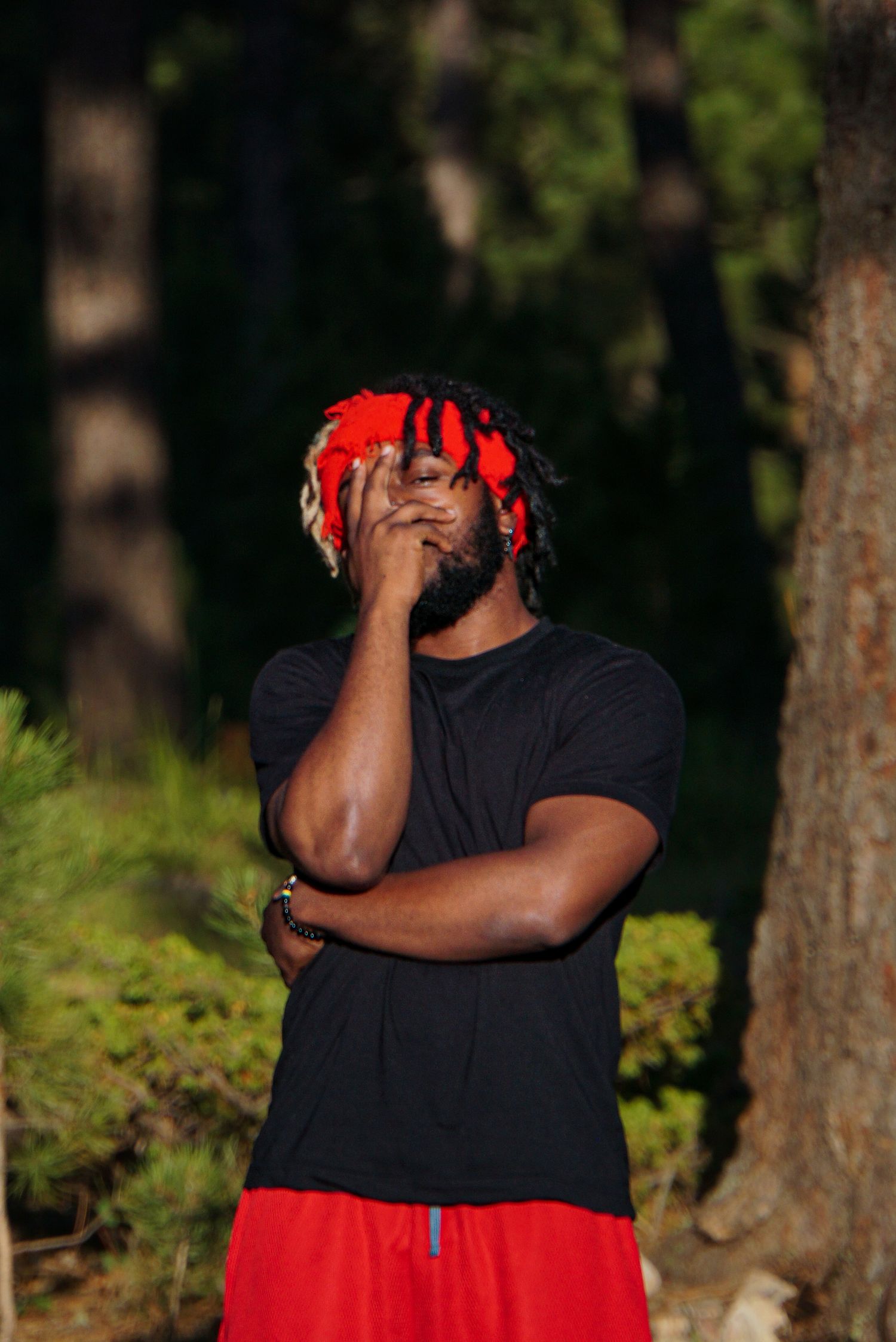Person in black shirt and red pants poses outdoors among pine trees.