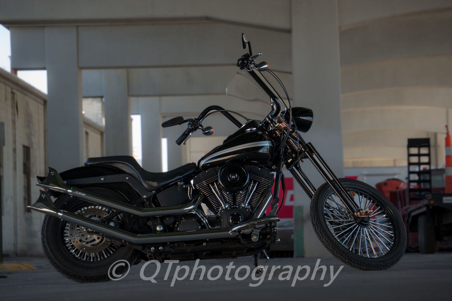 Custom black motorcycle photographed under concrete pillars with dramatic shadows.