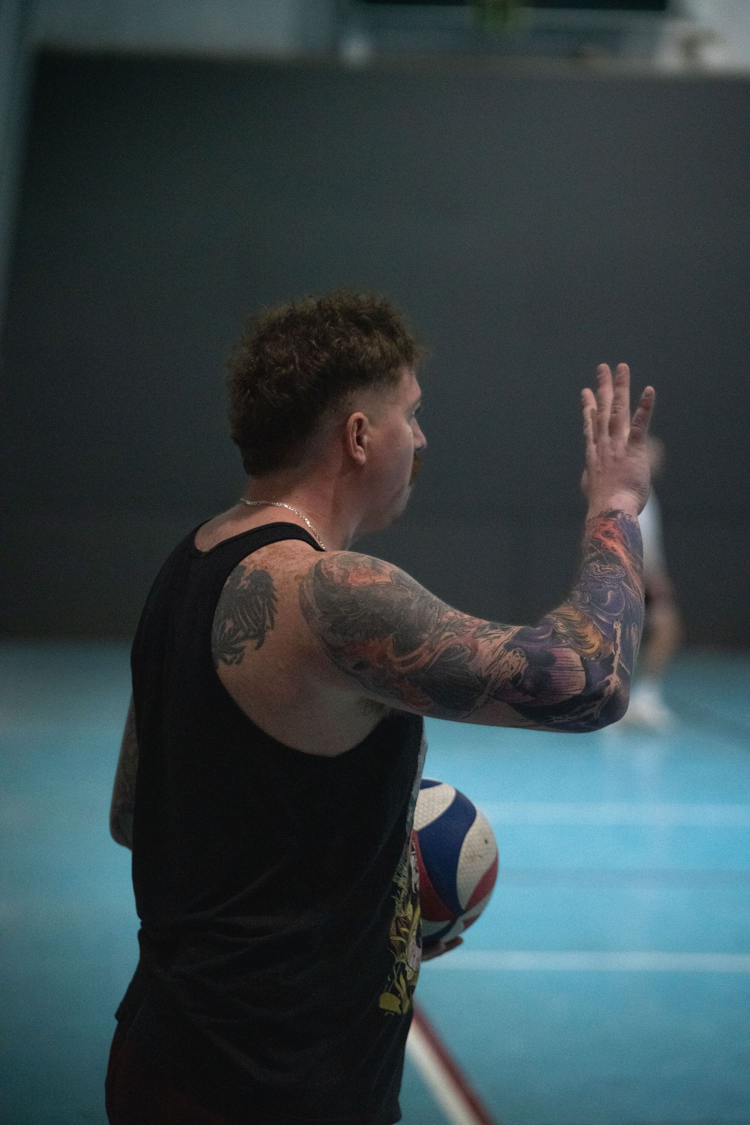 Tattooed athlete practicing volleyball moves in an indoor gym.