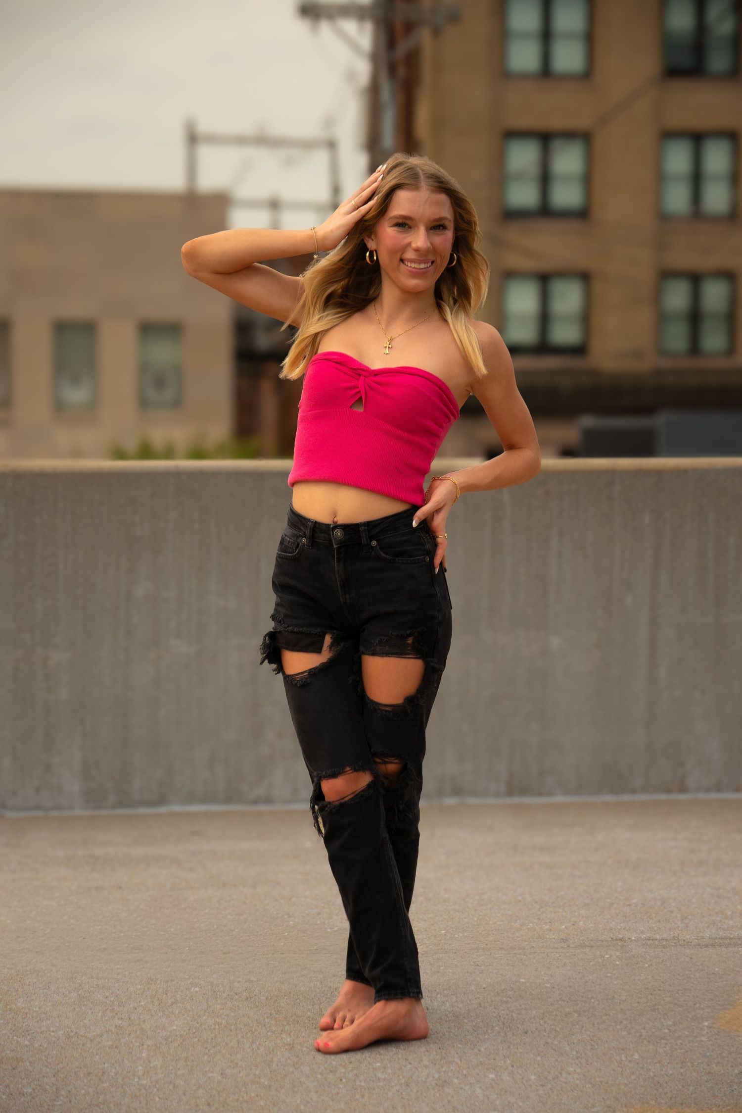 Dance poses in ripped black jeans and pink top on concrete rooftop.