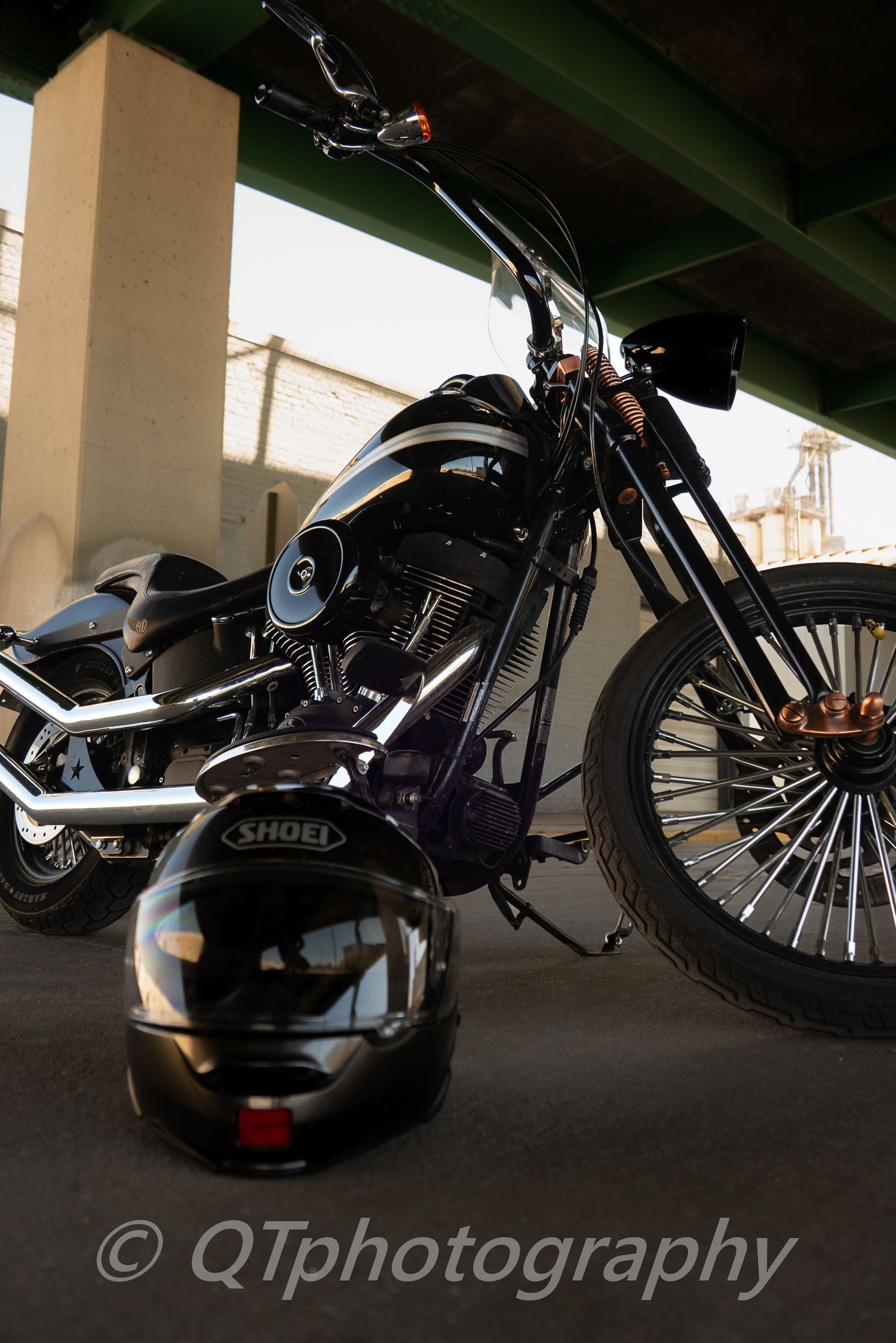 Low-angle shot of a black custom motorcycle under an overpass with dramatic shadows.