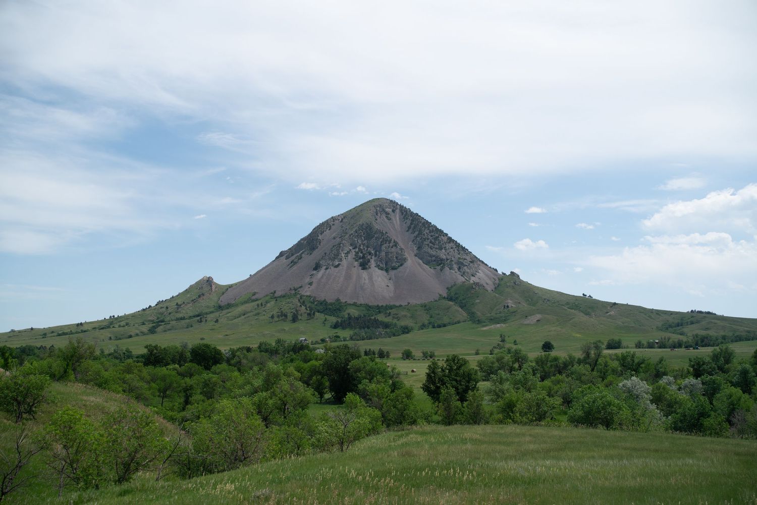 Panoramic landscape view of green hills and mountain peaks under blue sky.