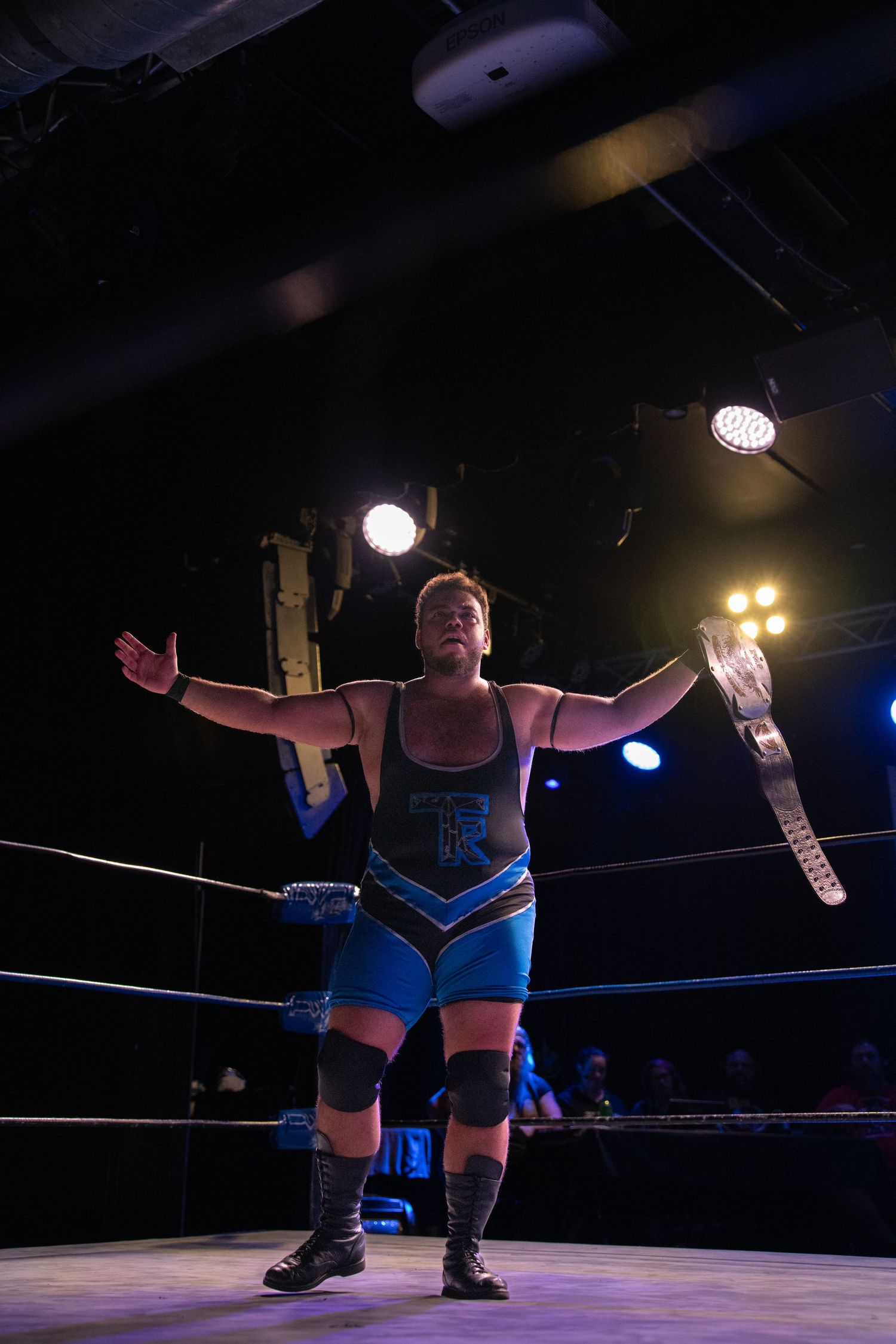 Wrestler in blue attire striking a dramatic pose in the wrestling ring.