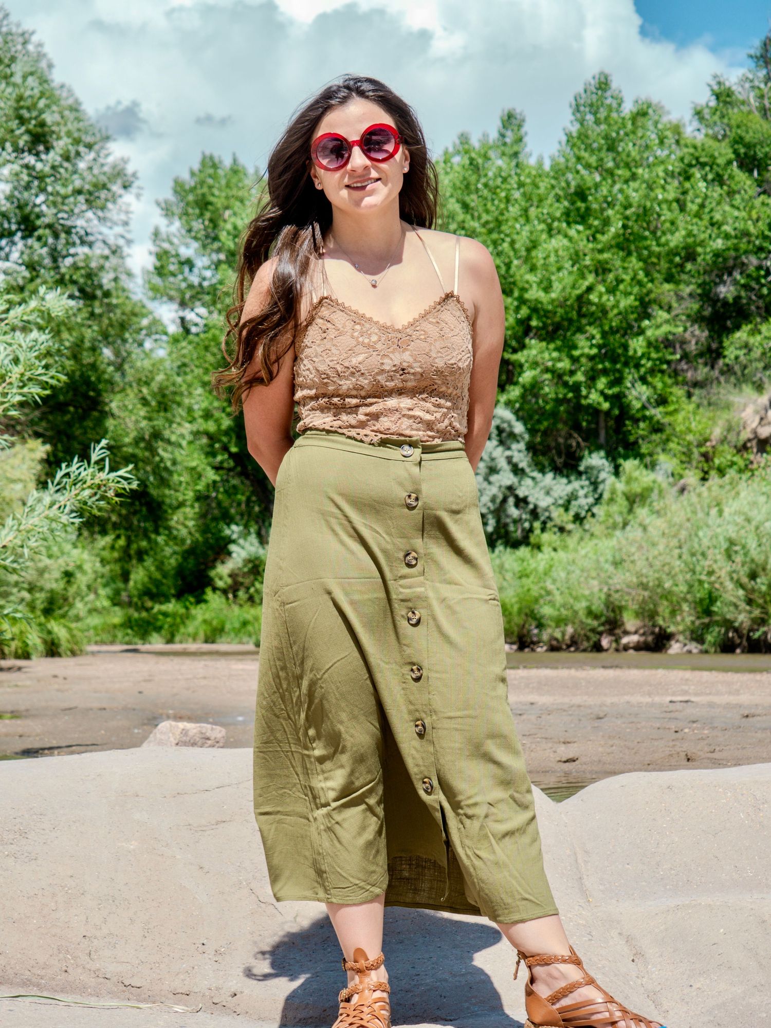 Summer fashion outfit featuring a lace crop top, olive button-down midi skirt, sunglasses and strappy sandals in outdoor setting.