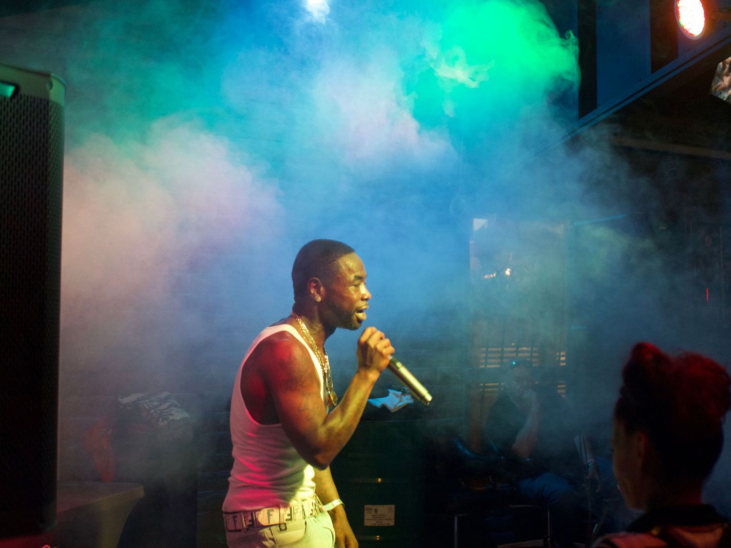 Performer in pink tank top sings on stage with dramatic teal and blue fog effects in the background.