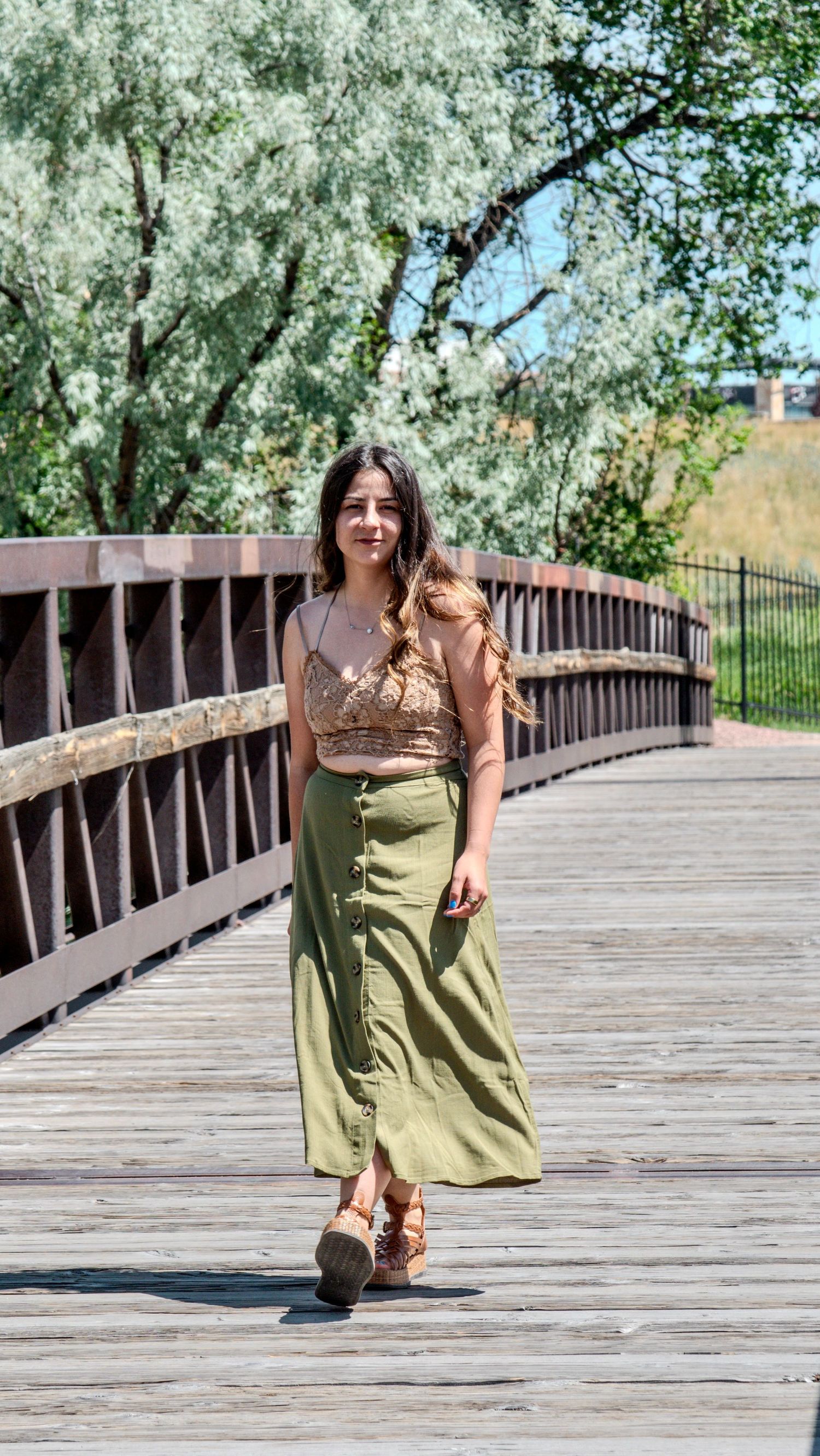 A sequence of motion photos showing someone in a flowing green dress walking along a wooden boardwalk on a sunny day.