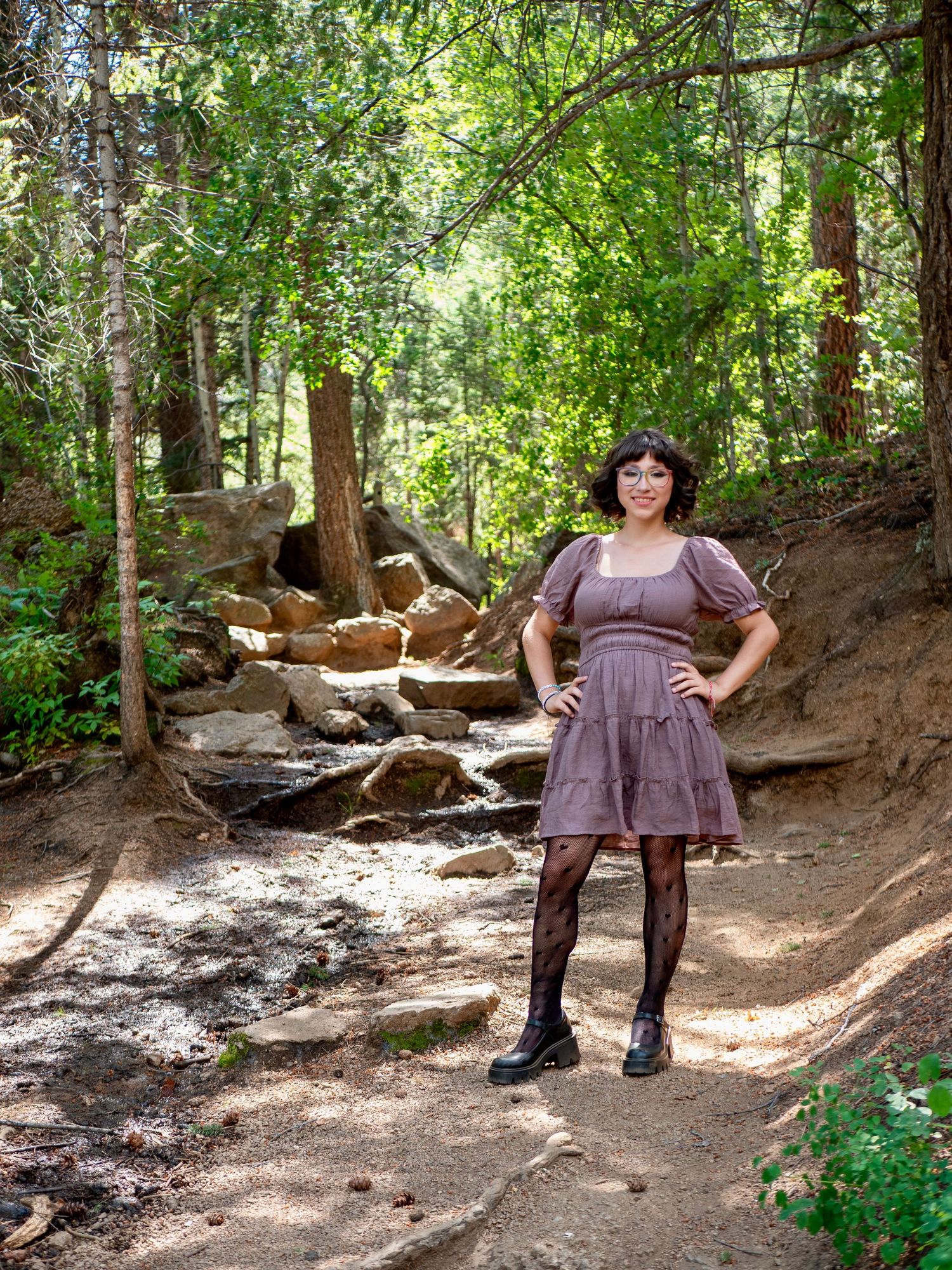 A collage of someone in a brown dress and boots standing in various poses on a wooded hiking trail dappled with sunlight.