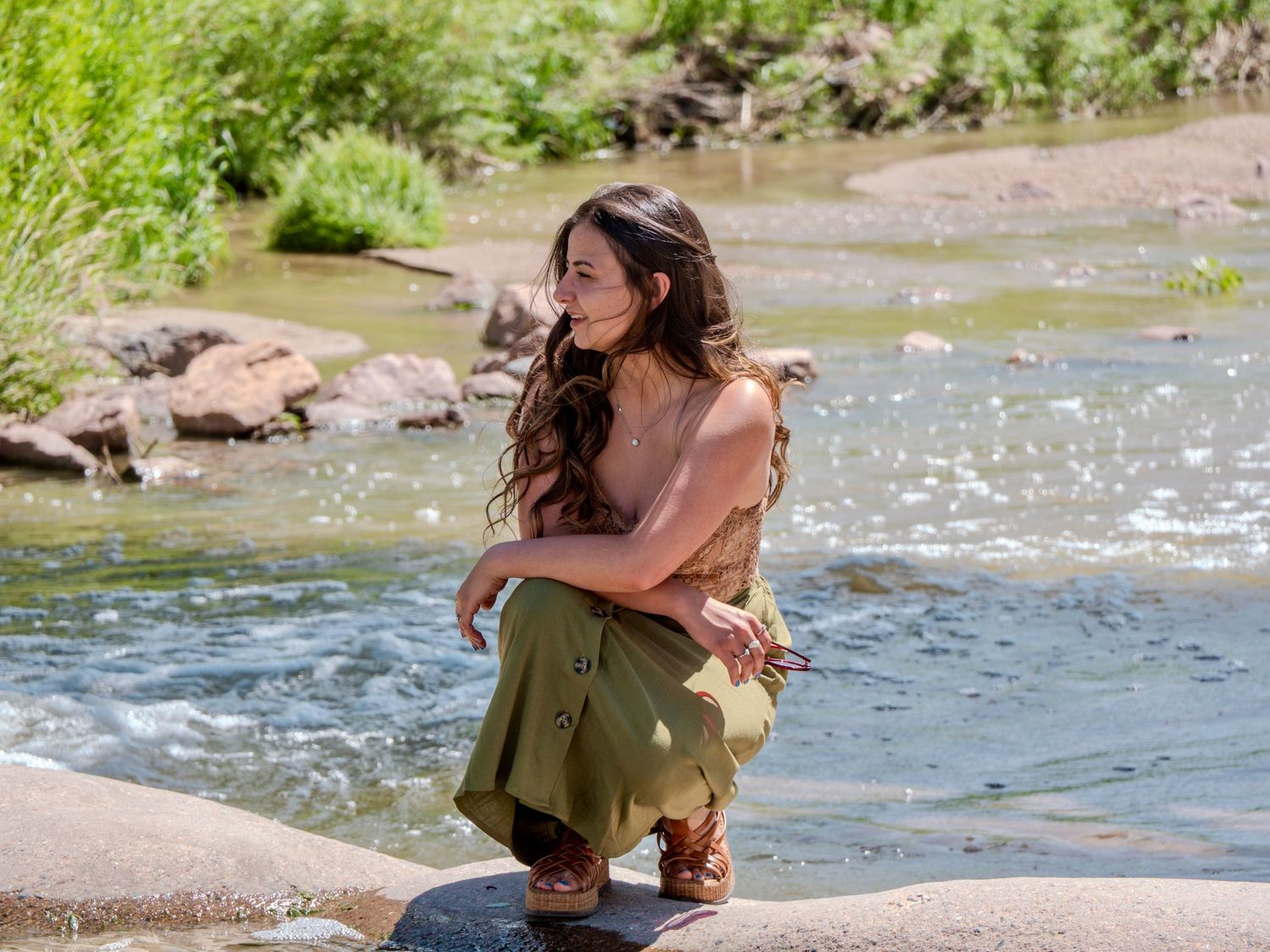 A figure wades in a rushing stream surrounded by rocks on a sunny summer day.