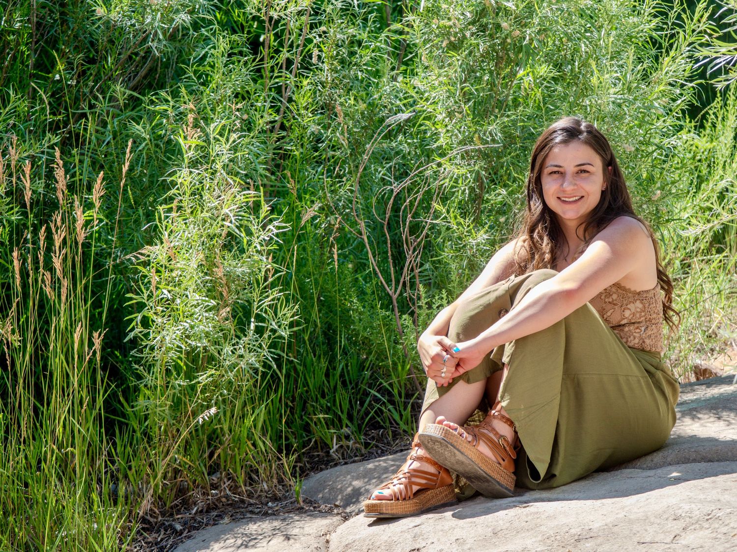 A figure in olive green lounges gracefully on rocks amidst lush bamboo foliage on a sunny afternoon.