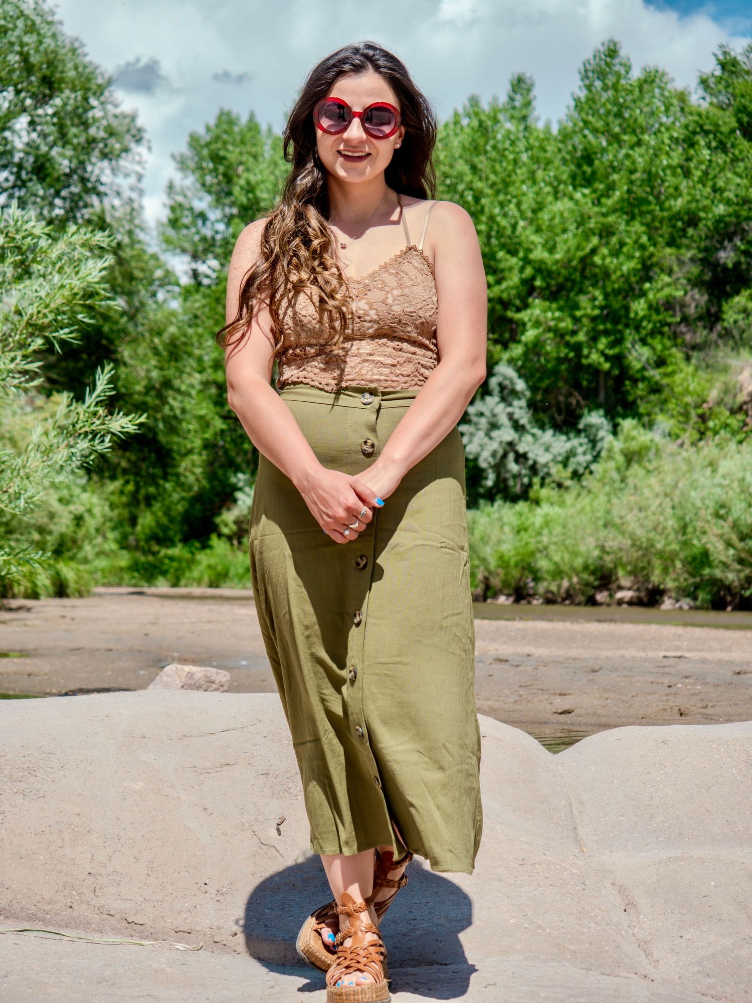 Summer fashion outfit featuring lace crop top, olive maxi skirt, sunglasses and brown sandals in outdoor setting.