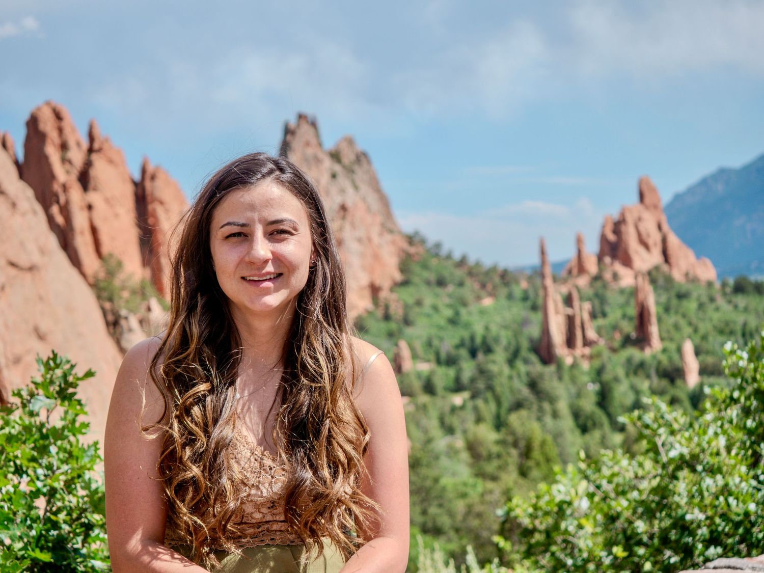 Rock formations tower over vegetation at Garden of the Gods park in Colorado on a sunny summer day.