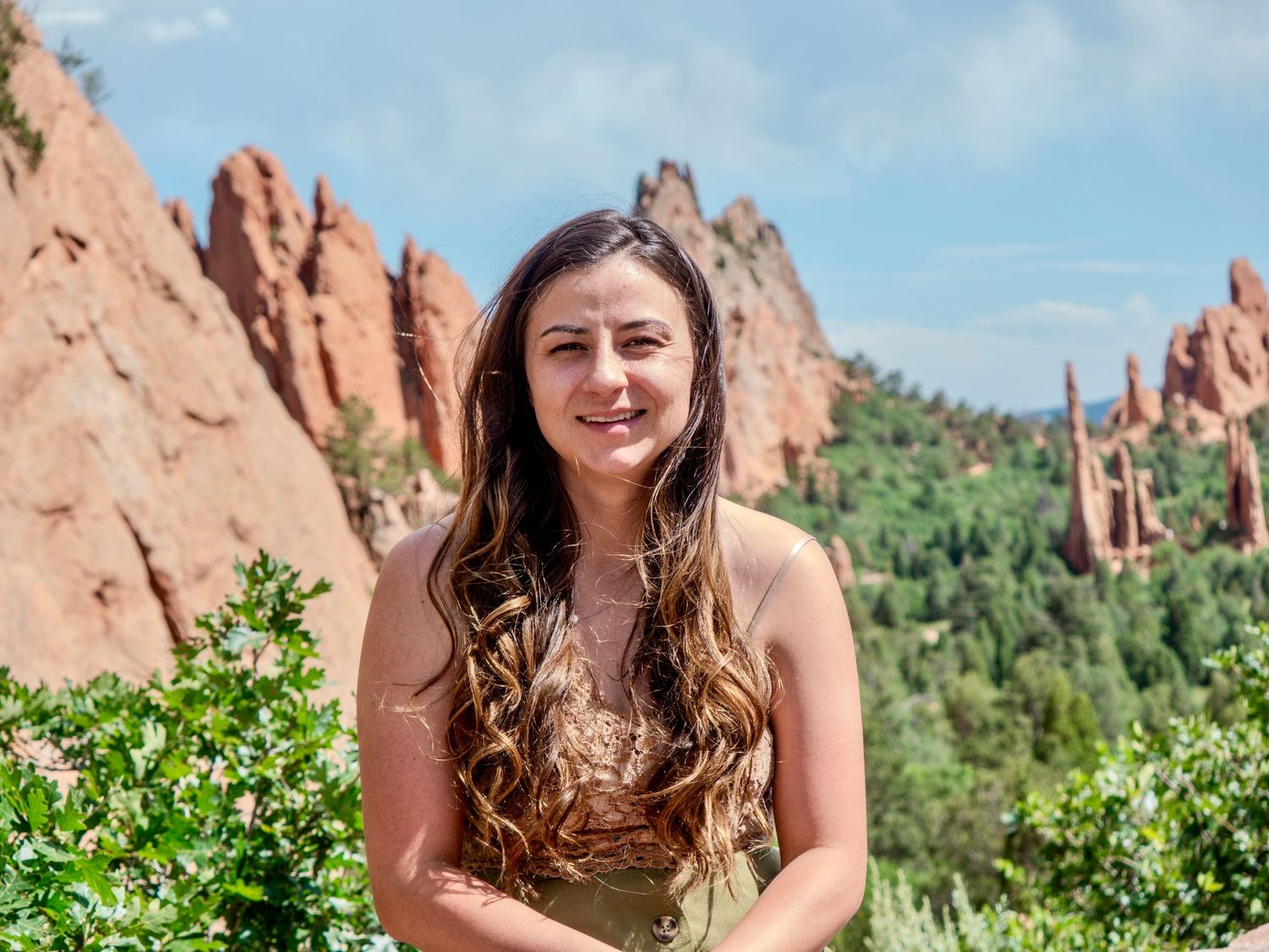 A person stands in front of striking red rock formations at Garden of the Gods park in Colorado on a sunny day.