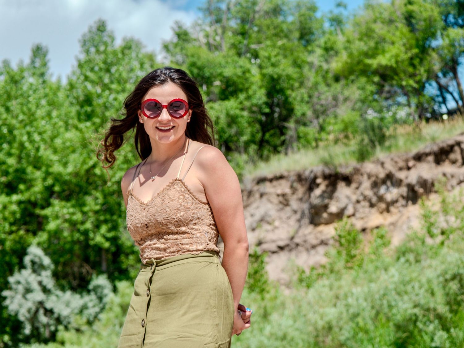 A woman in sunglasses walks along a grassy hill path on a sunny summer day.