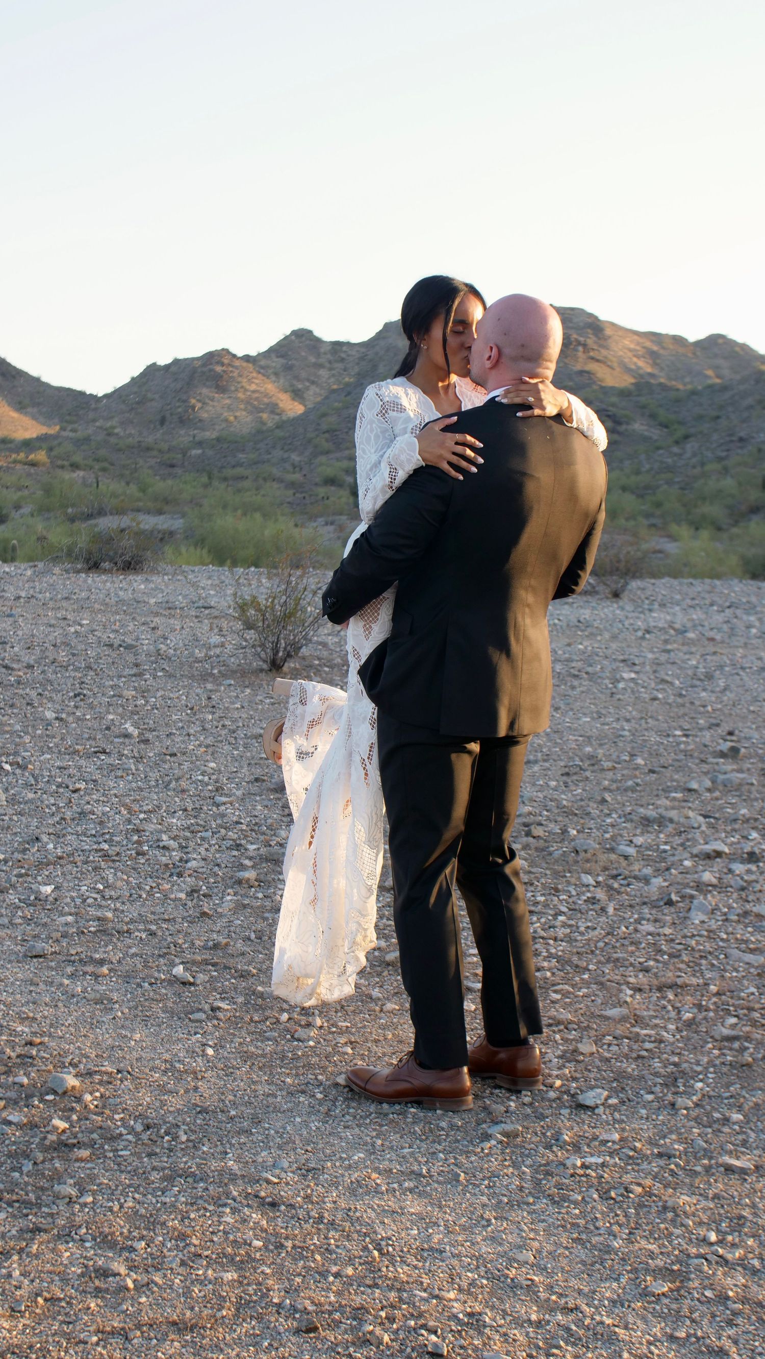 Two people embrace in a touching desert scene with mountains in the background.