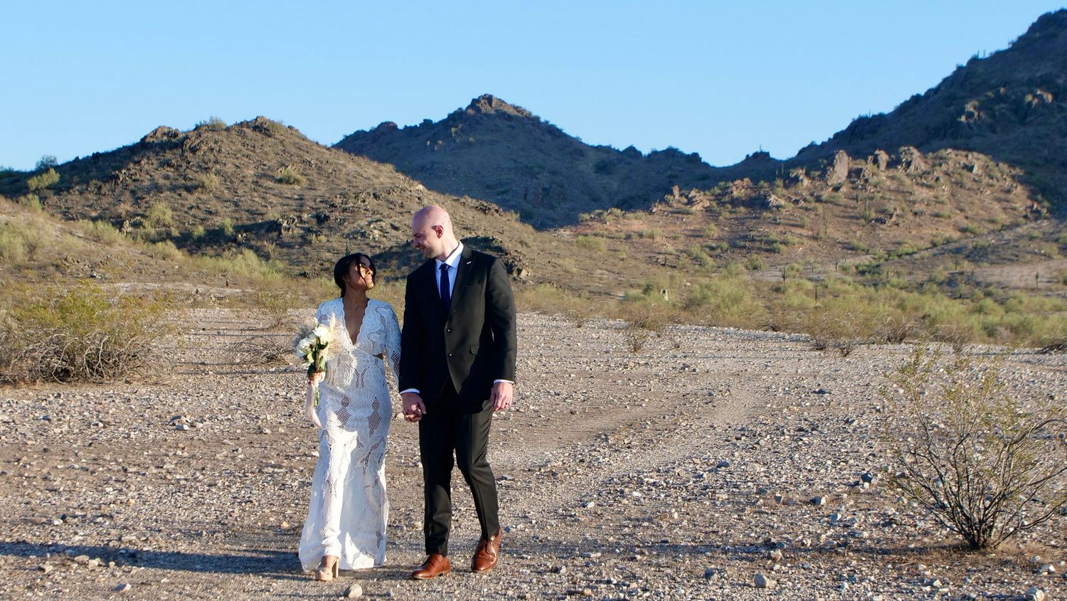 A couple in wedding attire poses together in front of dramatic desert mountain landscapes at various locations during sunset.