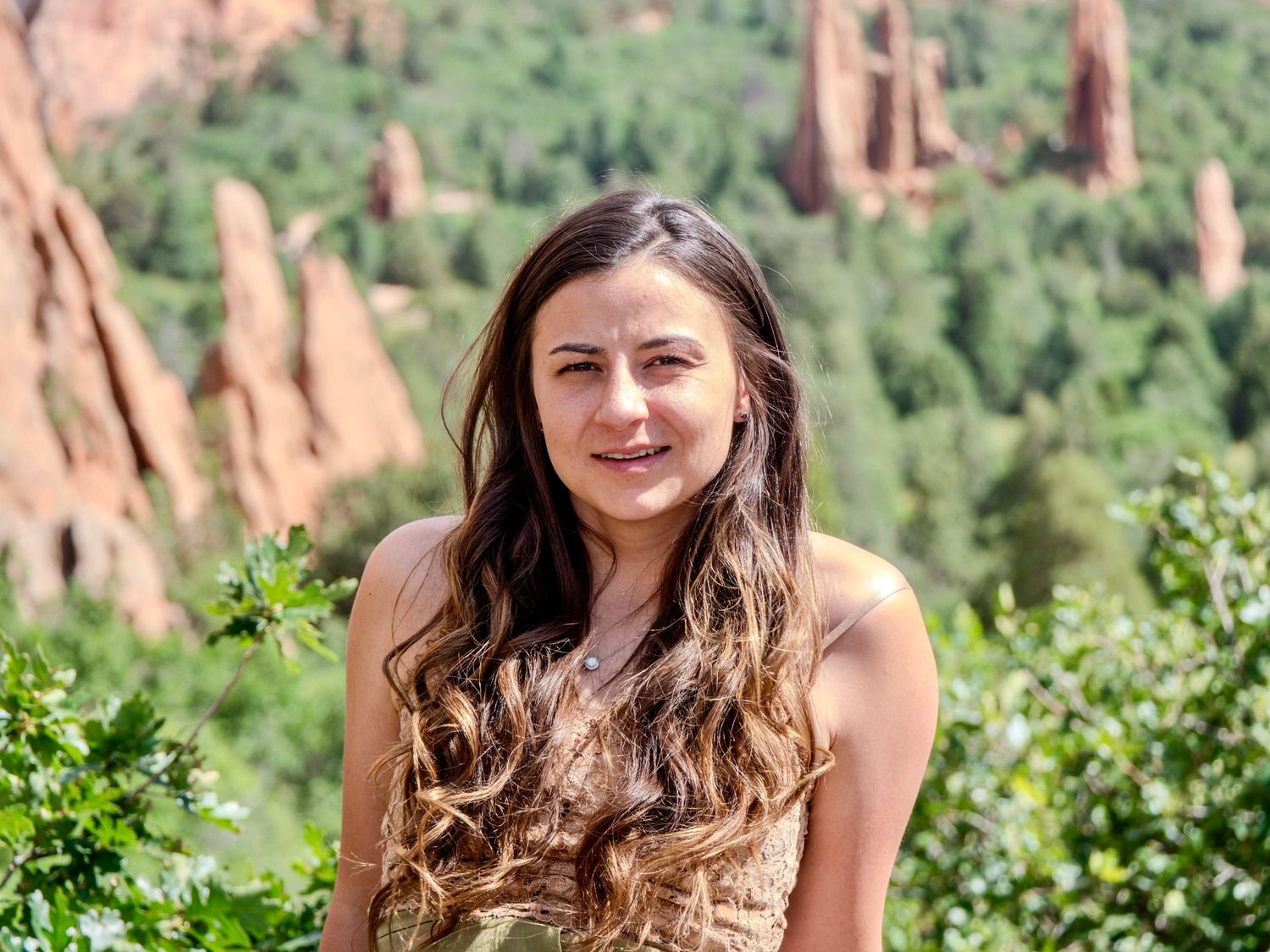 A person with brown hair smiles while enjoying scenic views of red rock formations at Garden of the Gods in Colorado.
