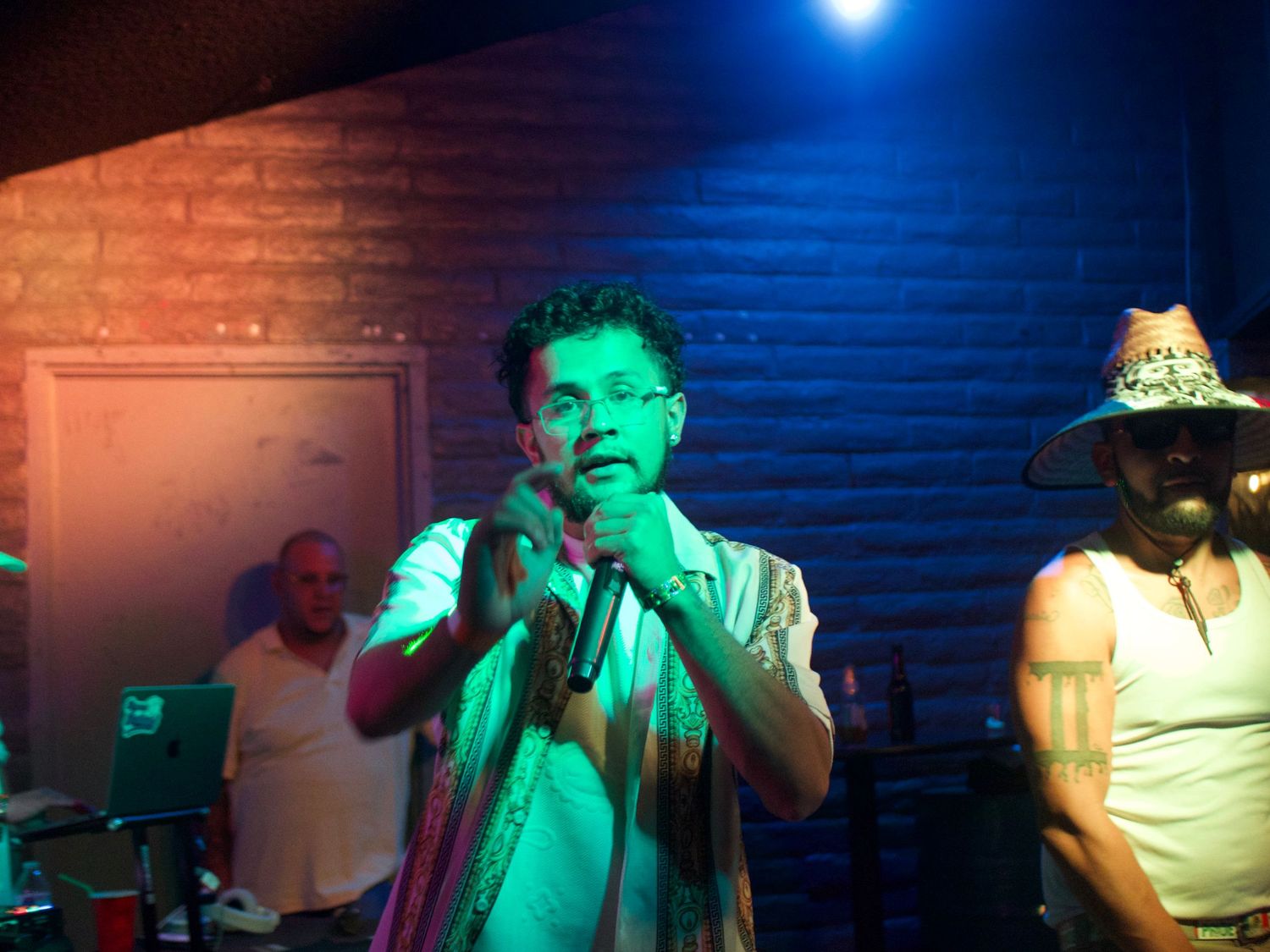 Performance footage at a music venue with dramatic blue and green stage lighting creates an atmospheric nightclub scene.