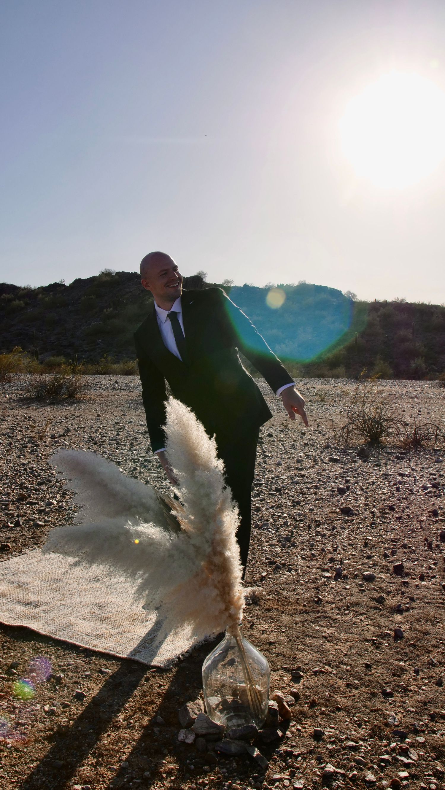 Person in business suit stomps on water bottle creating dramatic splash effect in desert landscape with sun flare.