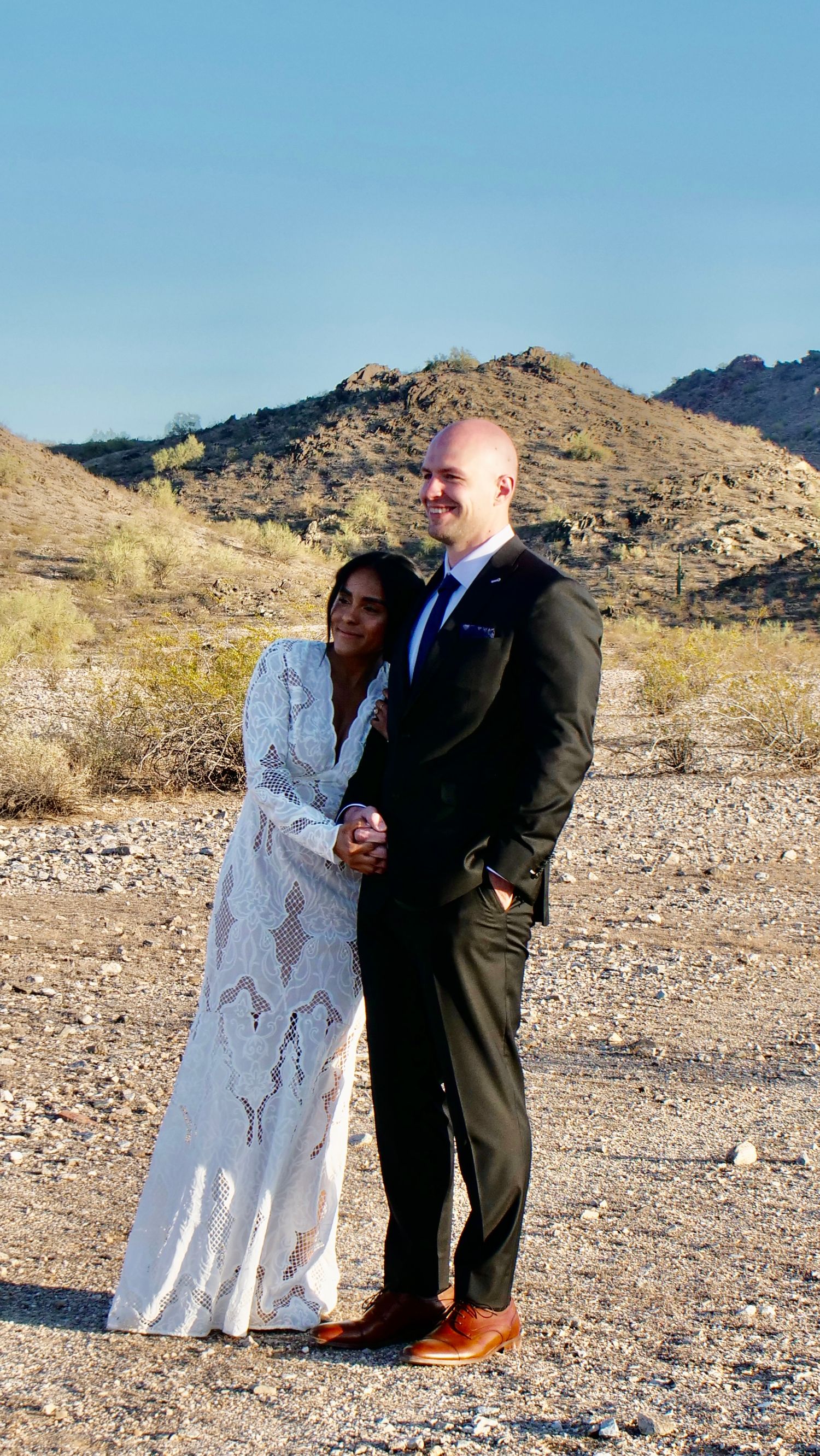 A marriage ceremony takes place in a desert landscape with mountains in the background on a sunny day.