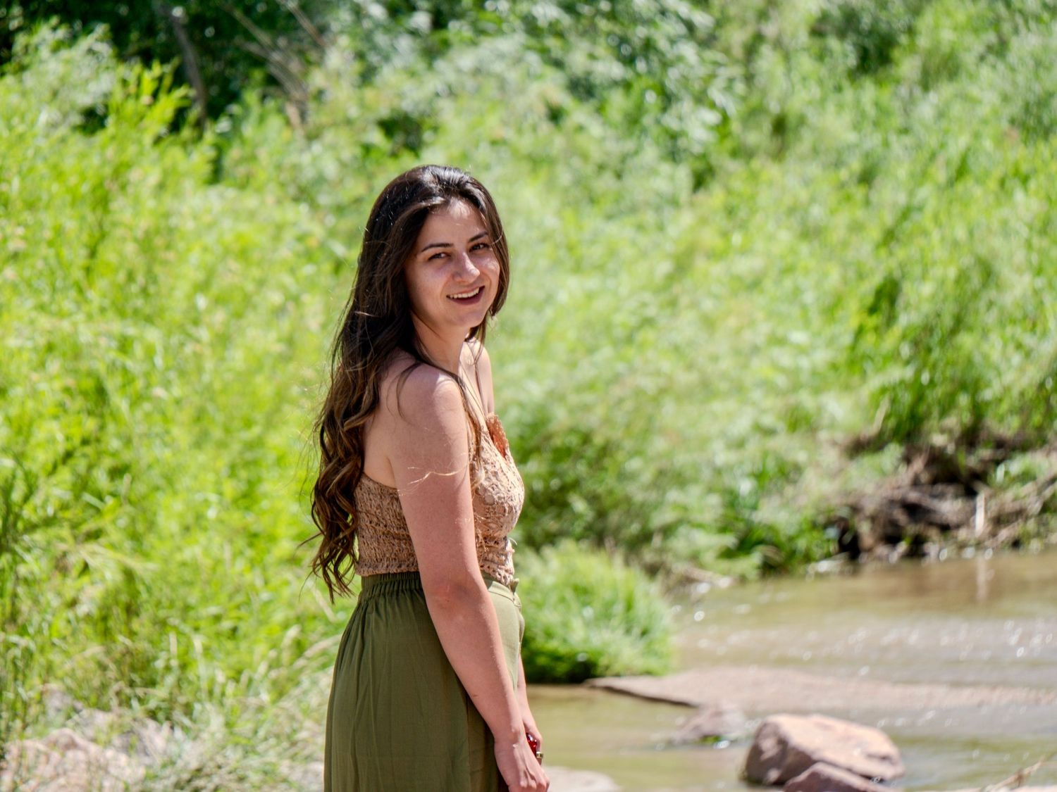 A person enjoying a summer day outdoors in casual clothing with lush green foliage in the background.