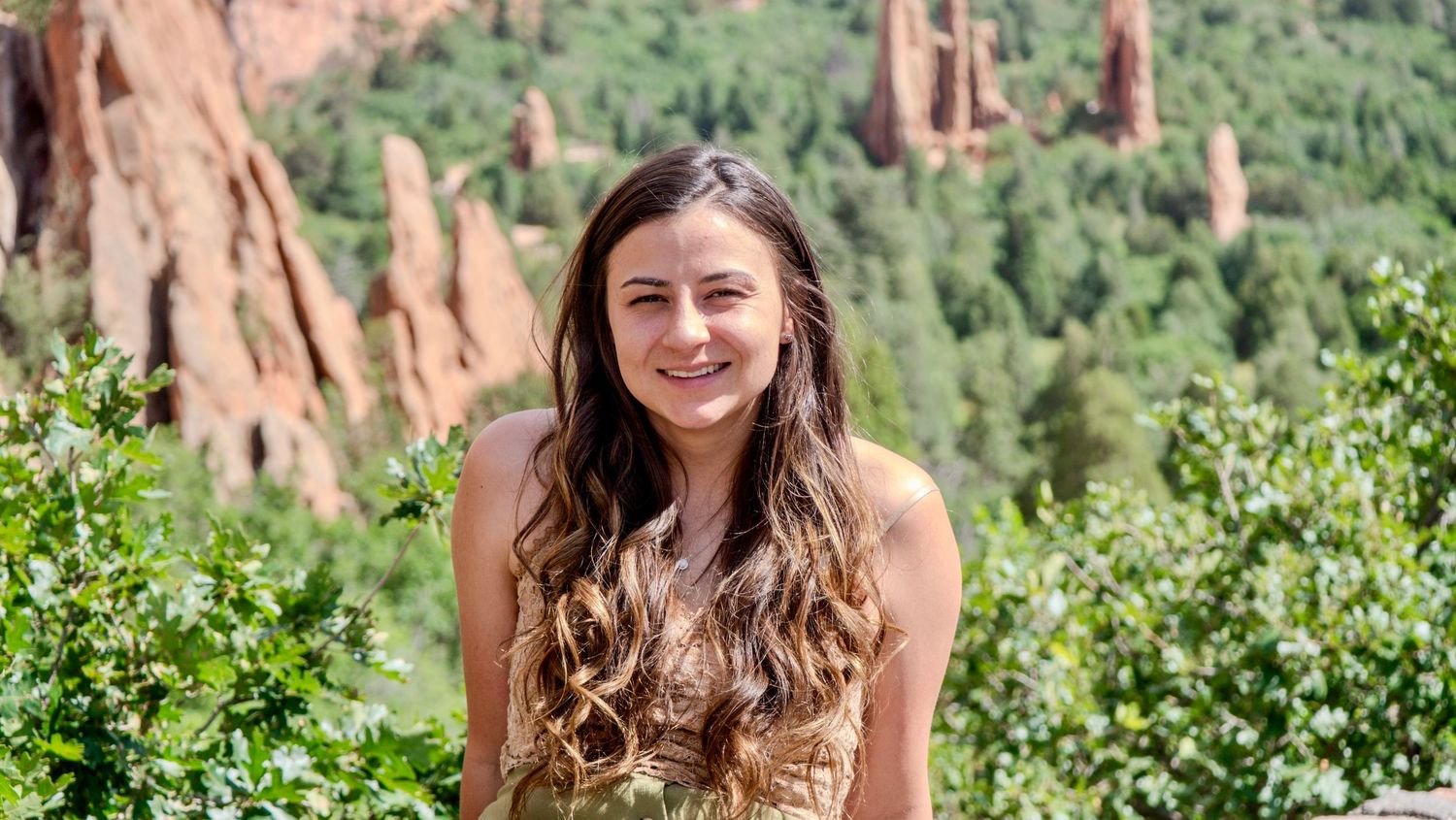 Young person smiling outdoors at Garden of the Gods park in Colorado with red rock formations in background.