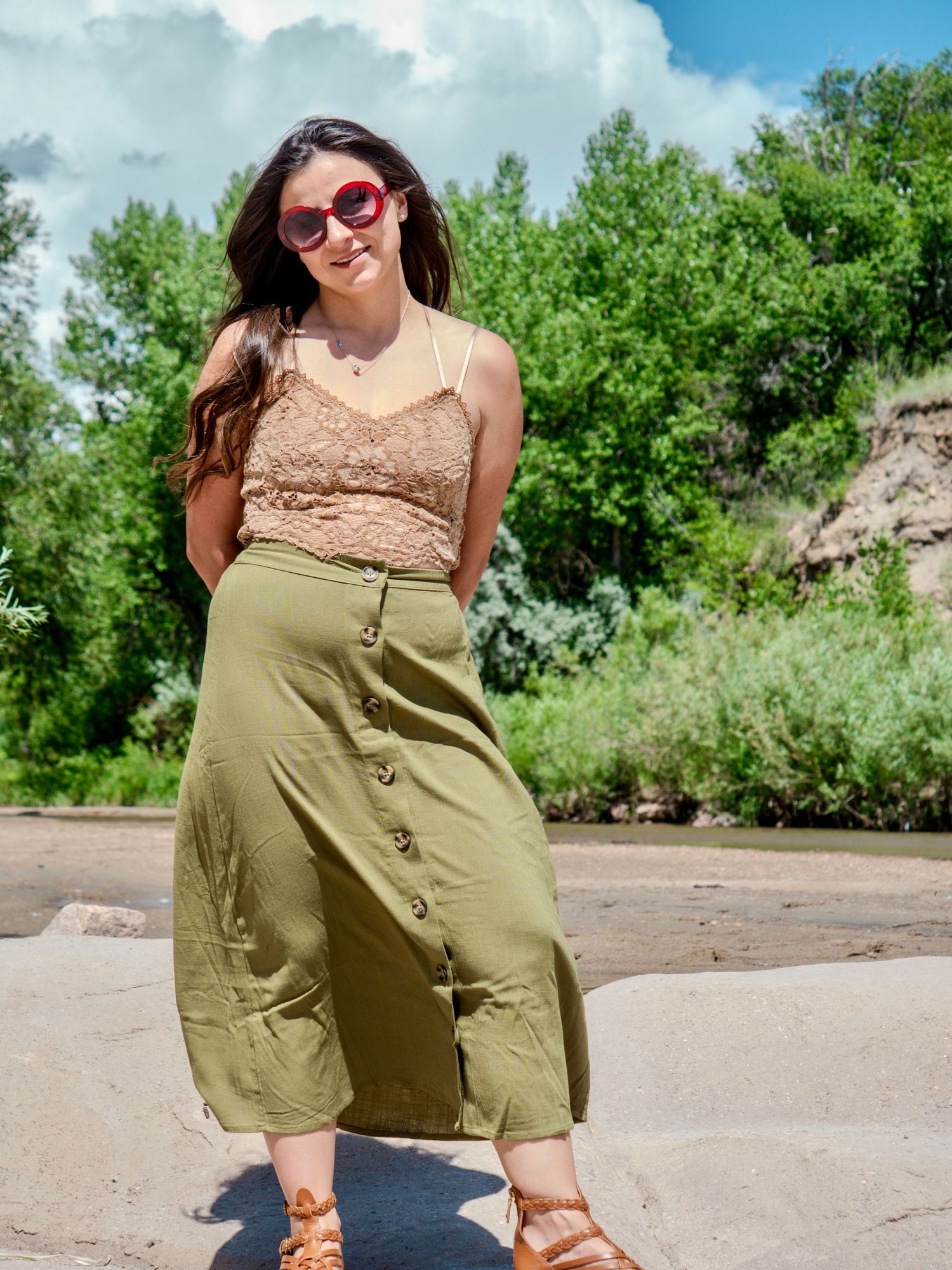Fashionable spring outfit featuring a beige lace top with olive button-front midi skirt and red sunglasses in outdoor setting.