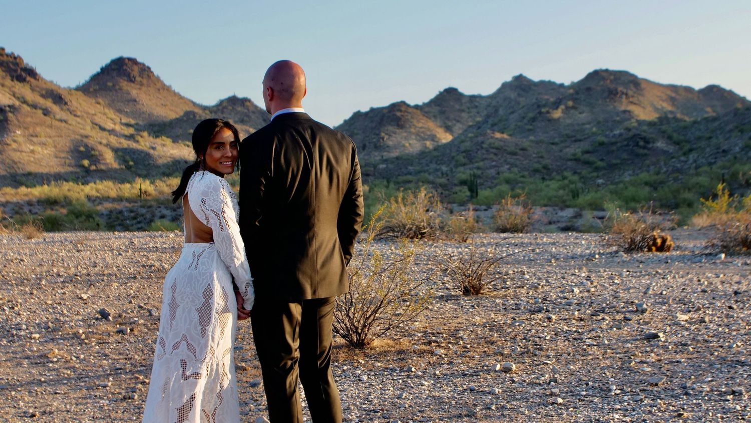 Wedding couple standing together in desert landscape with mountains in background.