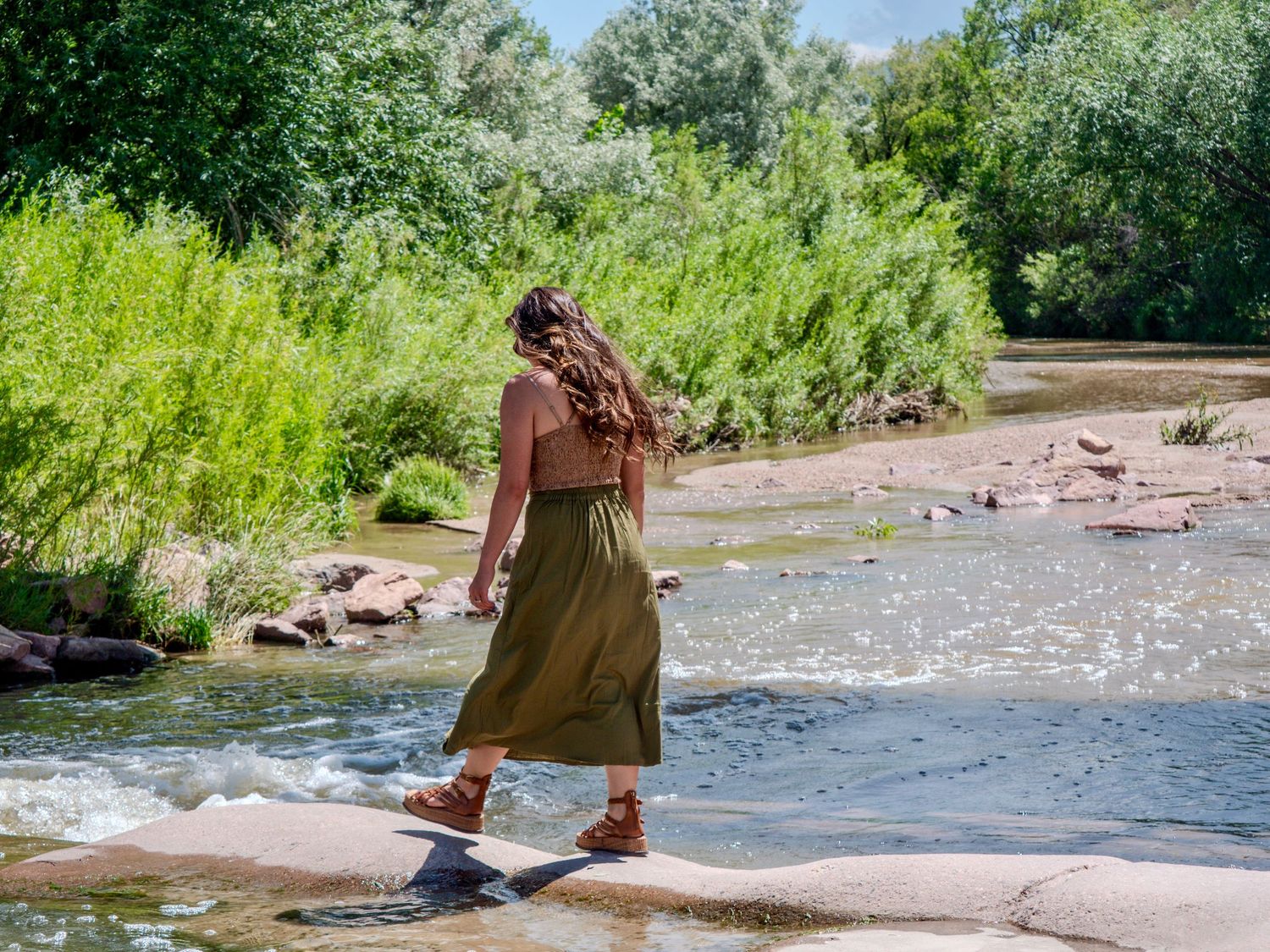 A series of connected photos showing people enjoying a sunny day by a flowing river with green foliage in the background.