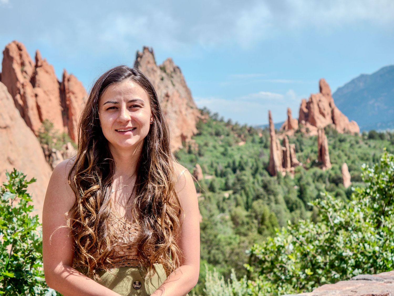 Person poses in front of the iconic red rock formations at Garden of the Gods park in Colorado Springs on a sunny day.
