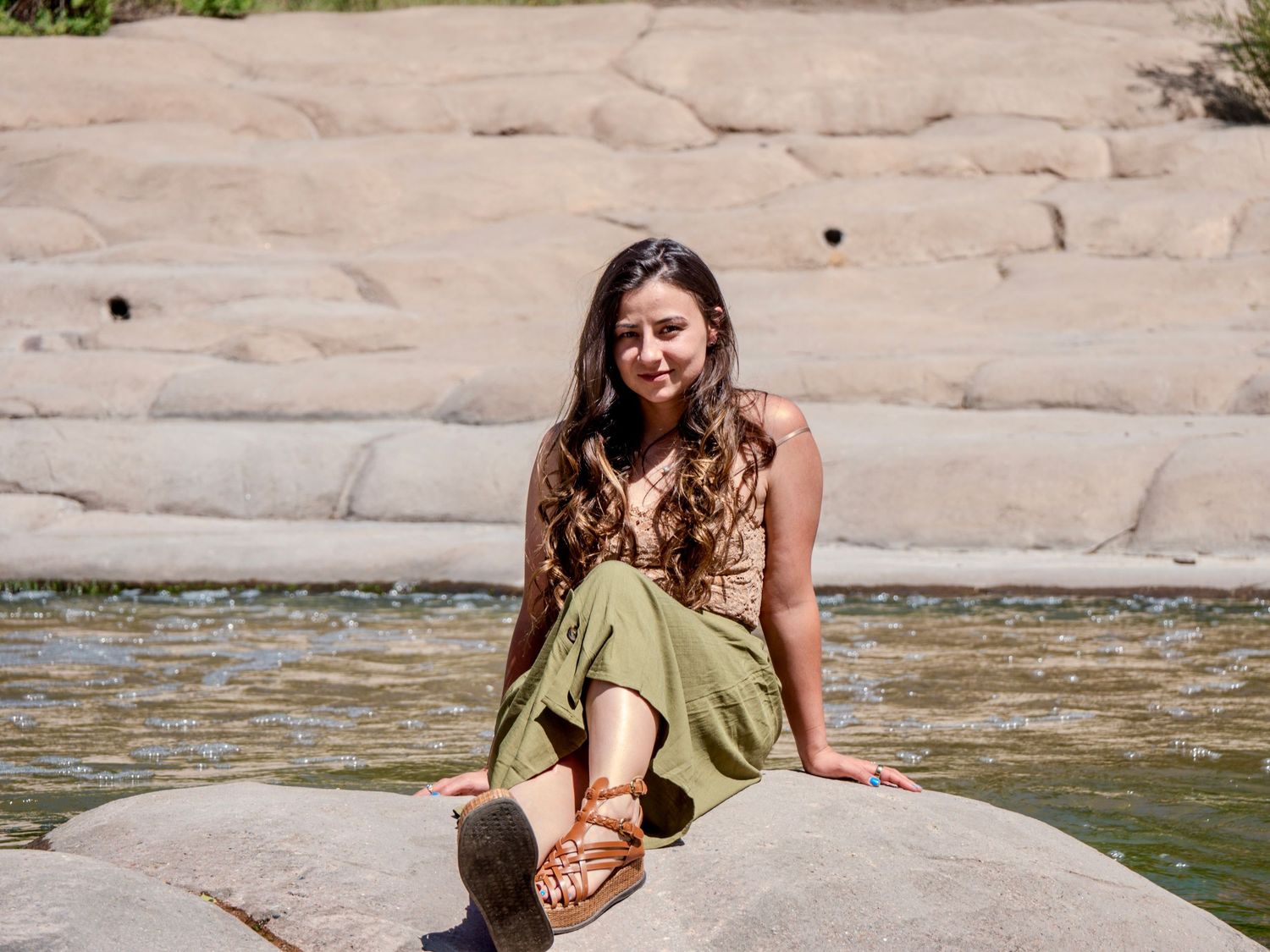 Someone soaks in crystal clear river water while resting against smooth rock formations on a sunny day.
