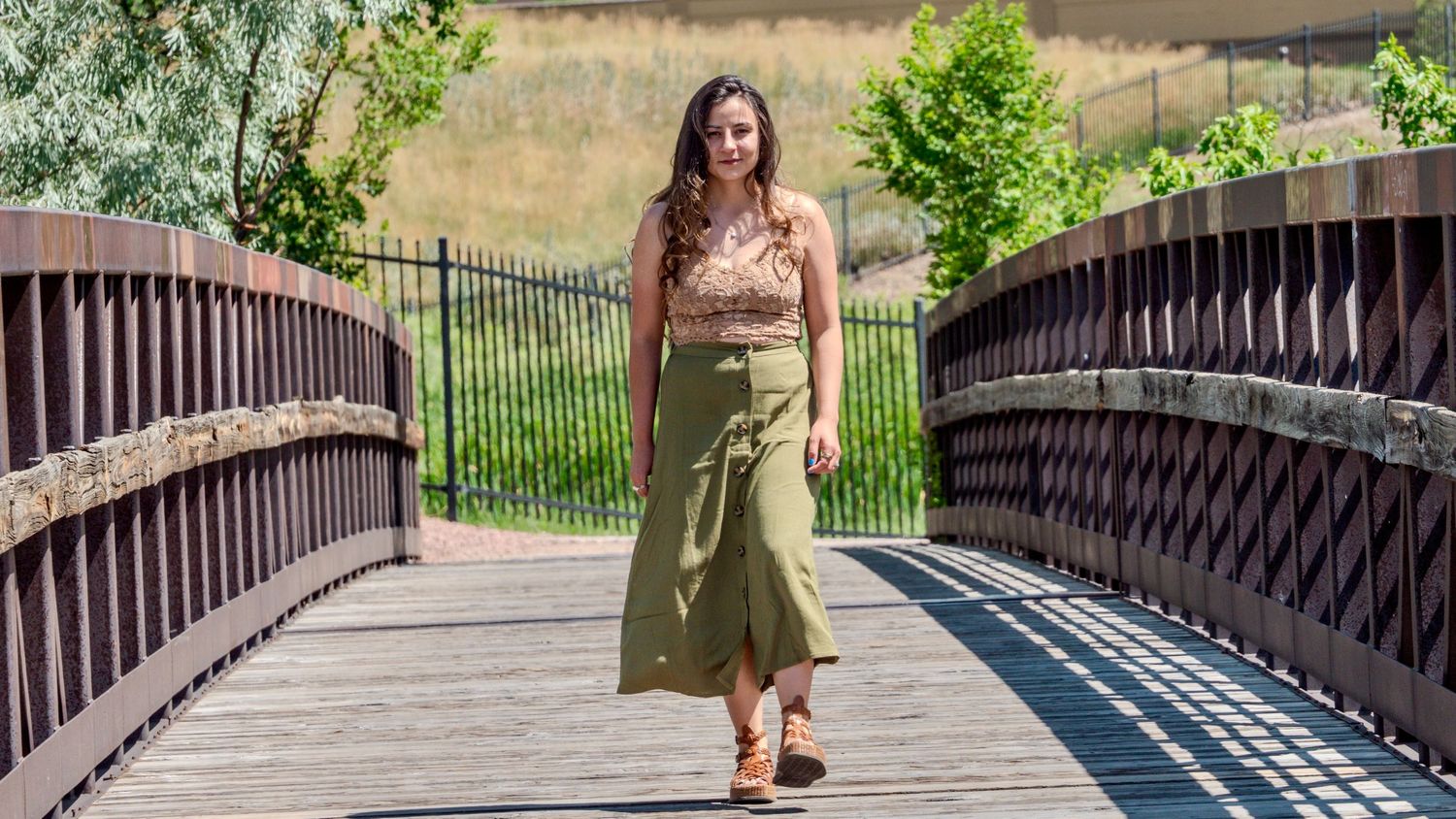 Someone wearing a floral crop top and olive midi skirt stands on a wooden bridge on a sunny day.