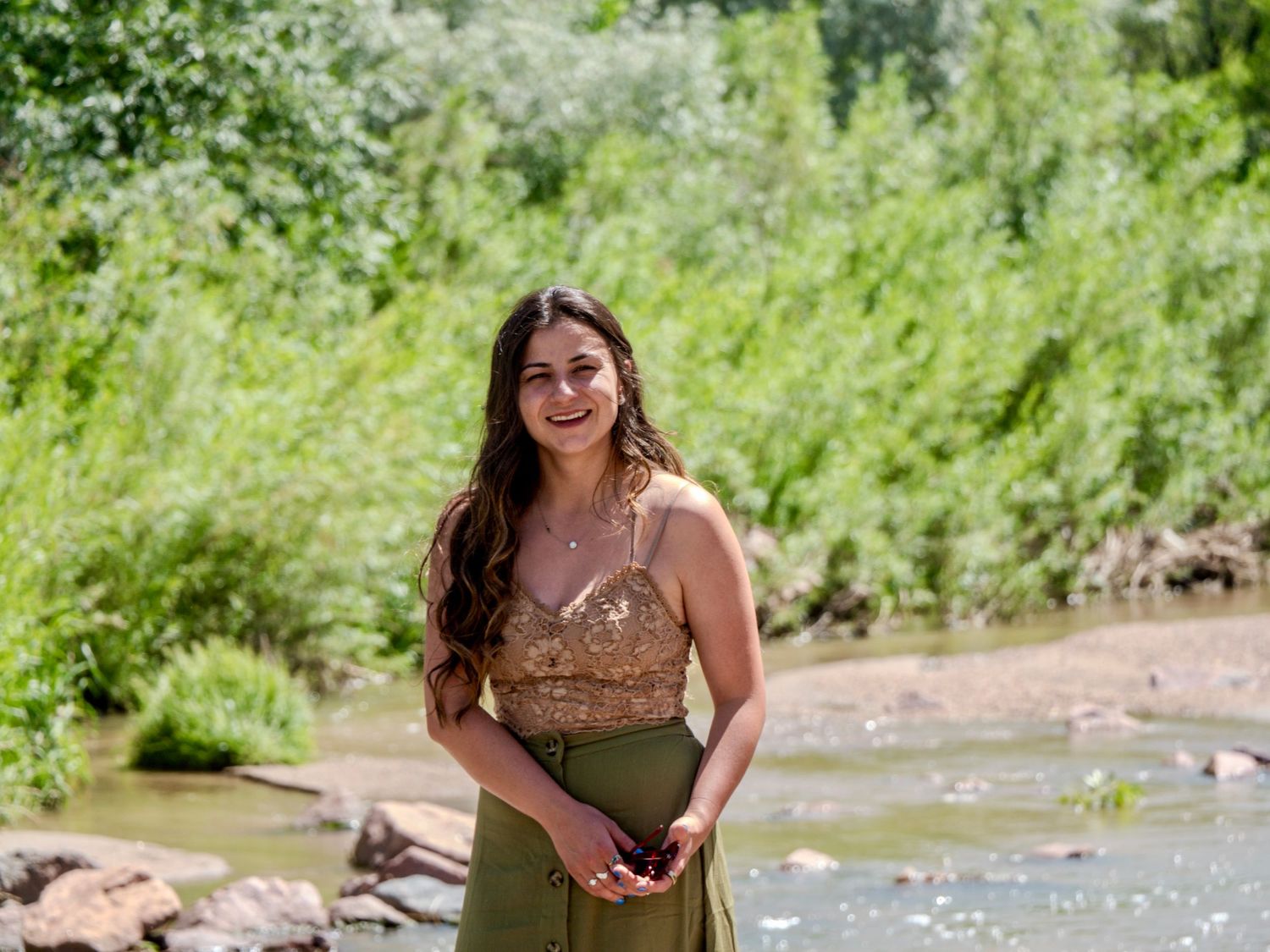 People enjoy a sunny summer day wading and swimming in a shallow creek surrounded by lush green foliage.
