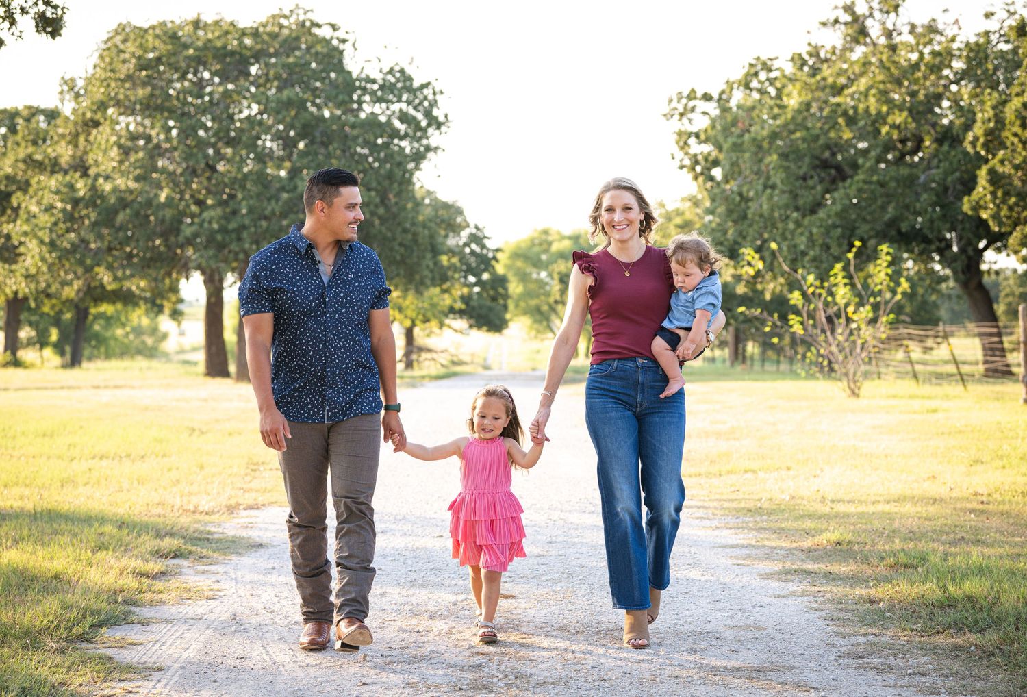 A family walks together on a sunlit path through an orchard during a bright summer day.