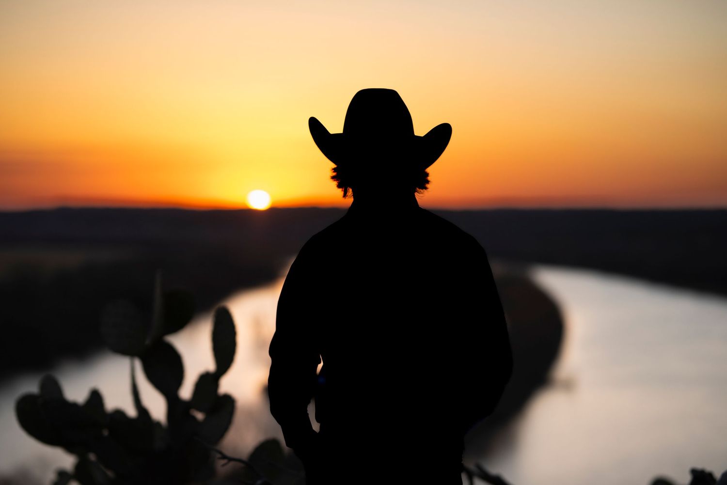 Silhouetted figures against a vibrant orange sunset over water.